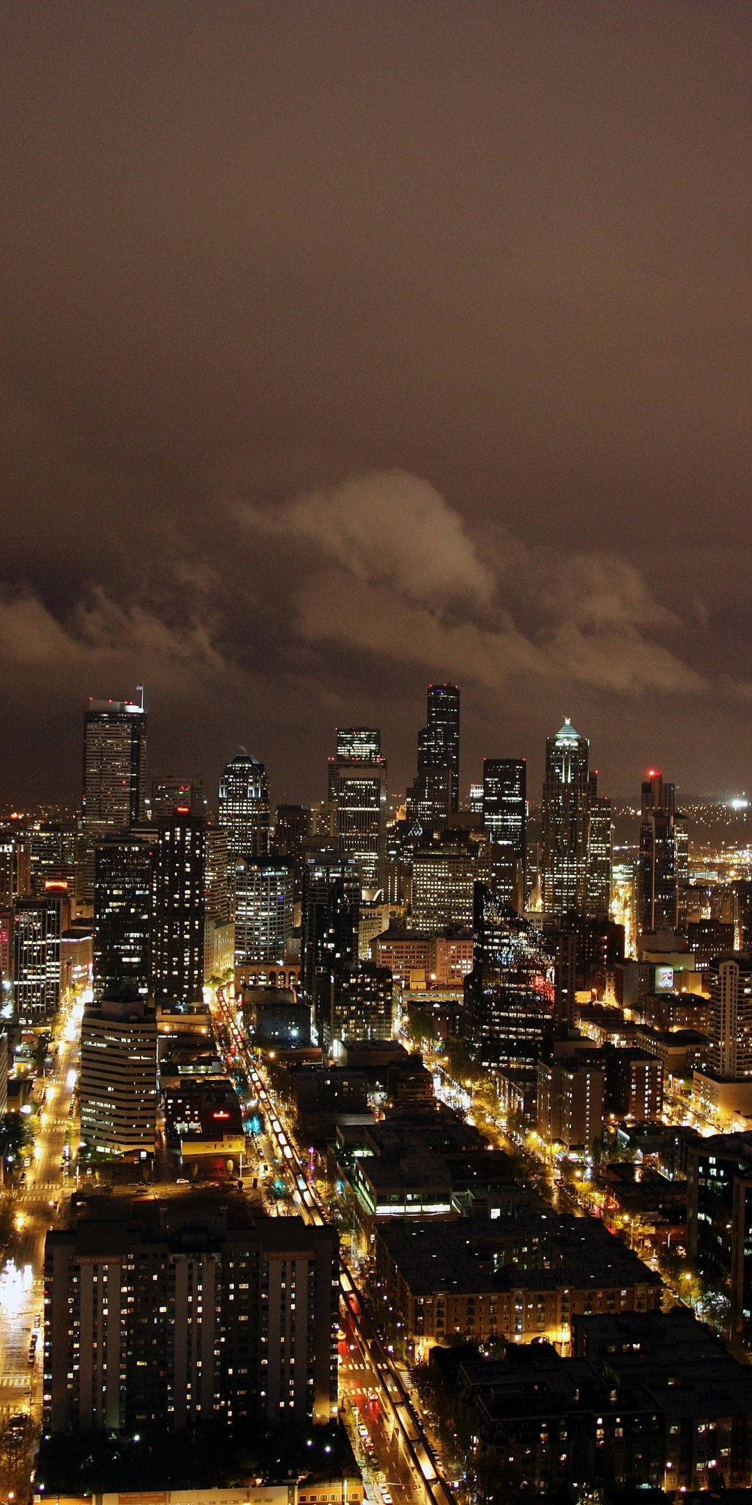 黃光夜景城市 壁紙 — 多雲天空下，閃爍摩天大樓和街燈的廣闊城市景觀的鳥瞰夜景。