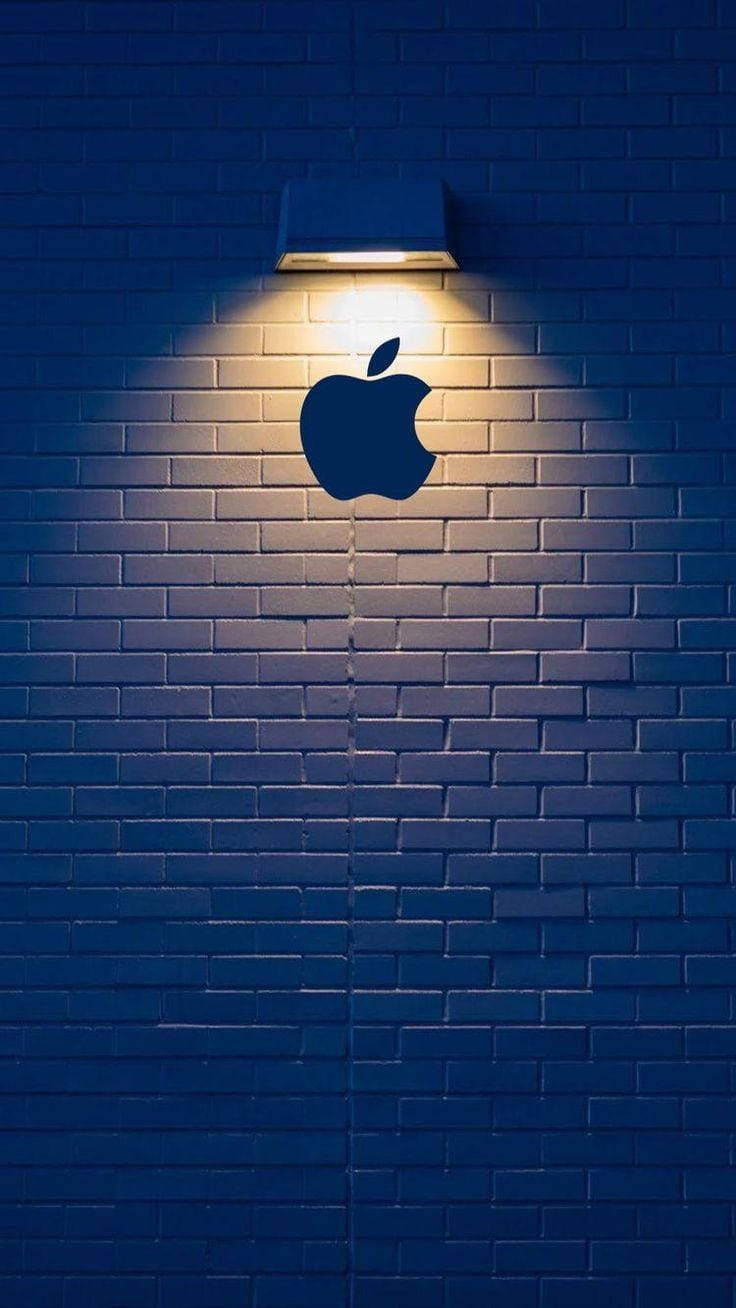 夜間，聚光燈照亮藍色磚牆上的Apple標誌輪廓。