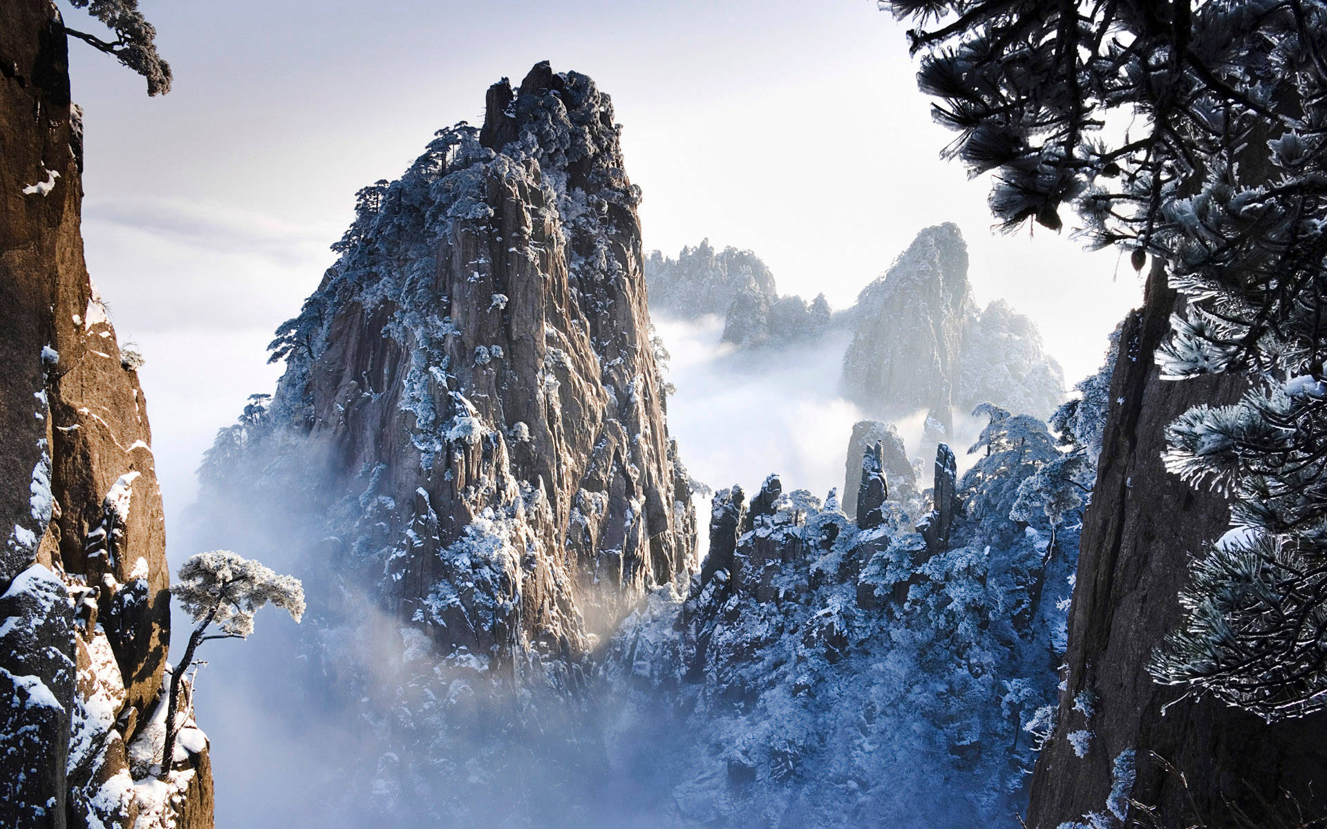 黃山雪峰 壁紙 — 白雪覆蓋著崎嶇的山峰和松樹，薄霧在山谷中盤旋。