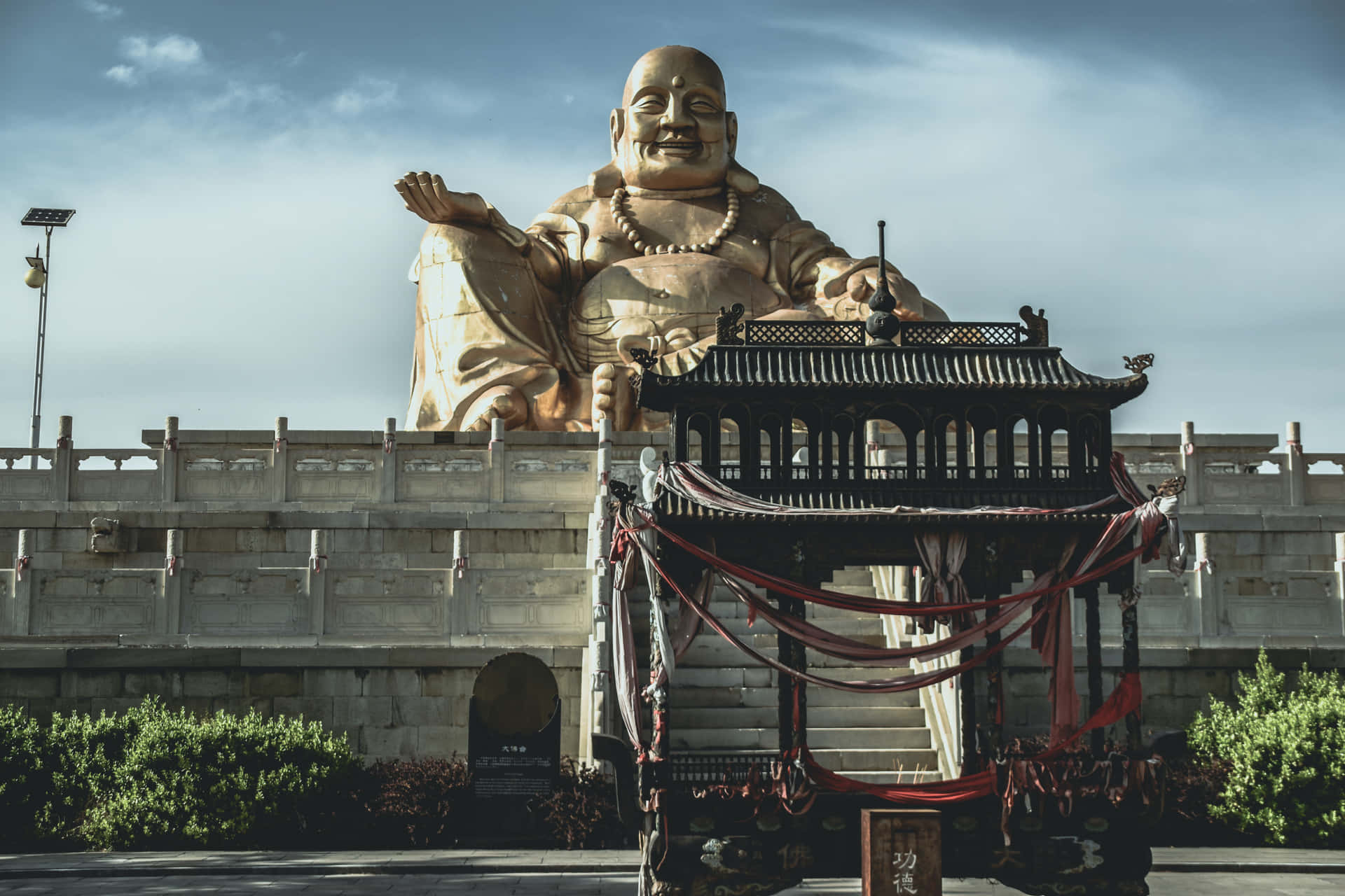 金色佛像與傳統亭子和紅色絲帶在寺廟環境中。