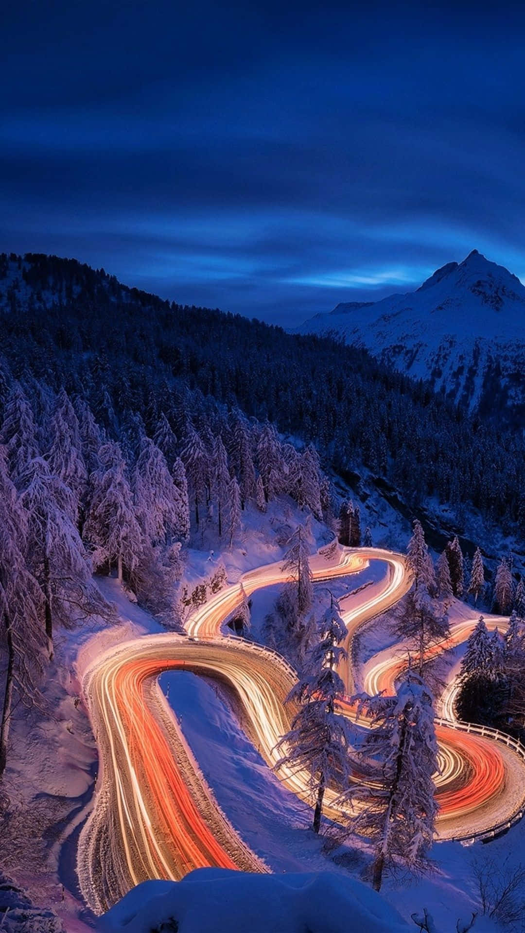 time lapse 桌布 壁紙 — 黃昏時分，一條蜿蜒的積雪山路，汽車的發光軌跡穿過結霜的松樹。