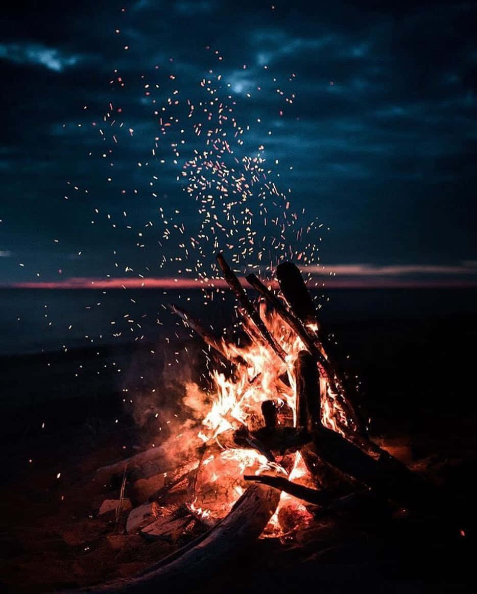 Beach Camping 桌布 壁紙 — 黃昏時分，咆哮的營火將火花射向水面上深藍色的暮色天空。
