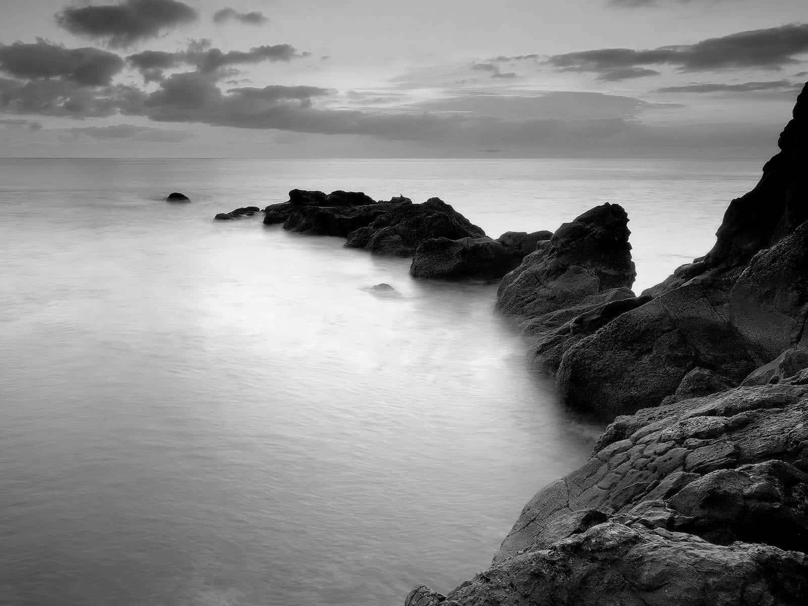 Black And White Landscape 桌布 壁紙 — 黃昏時分，在陰雲密布的天空下，光滑的水流繞過參差不齊的岩石，形成單色海景。