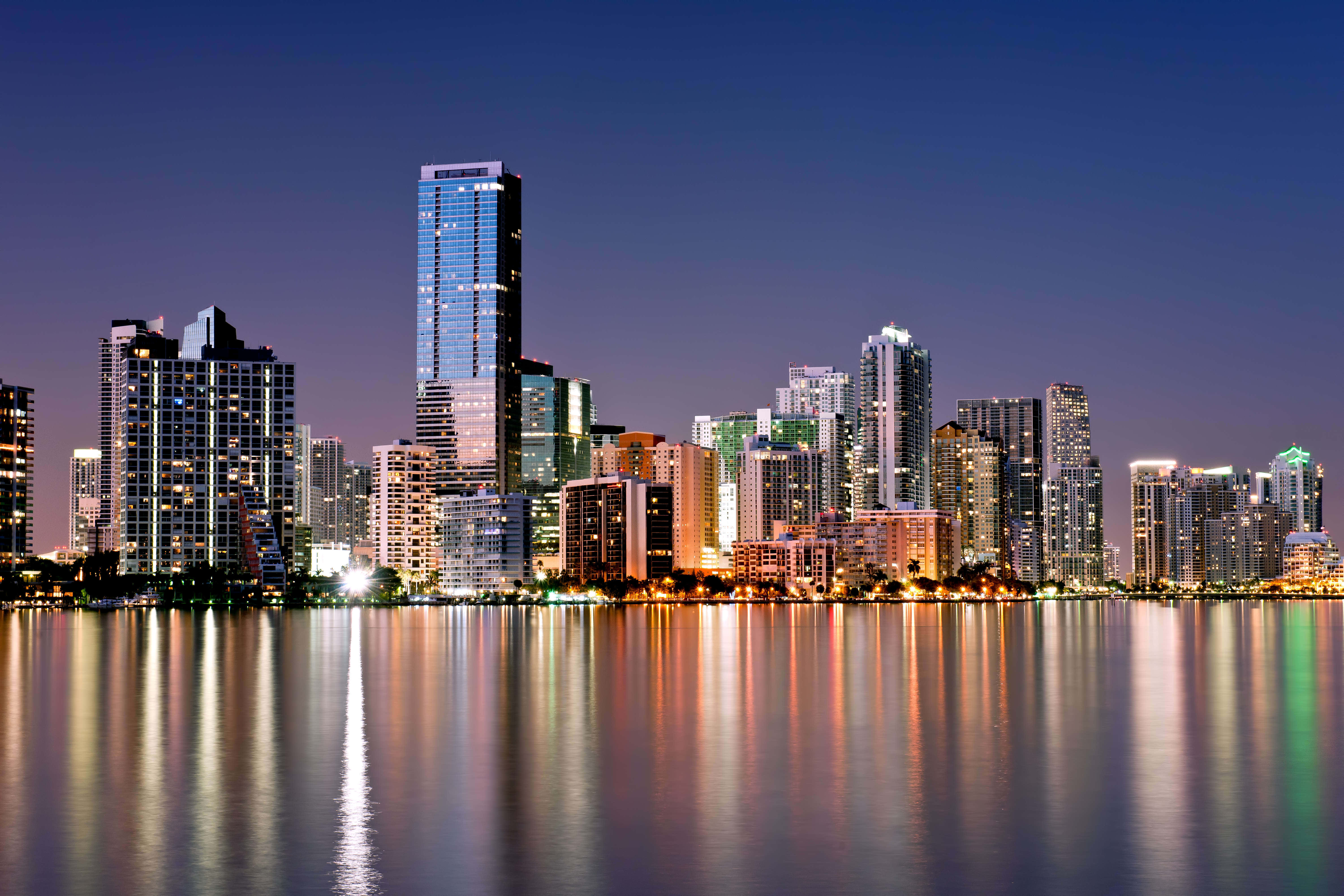Miami 桌布 壁紙 — 黃昏時分充滿活力的城市天際線，摩天大樓在平靜的水面上反射出五彩繽紛的燈光。