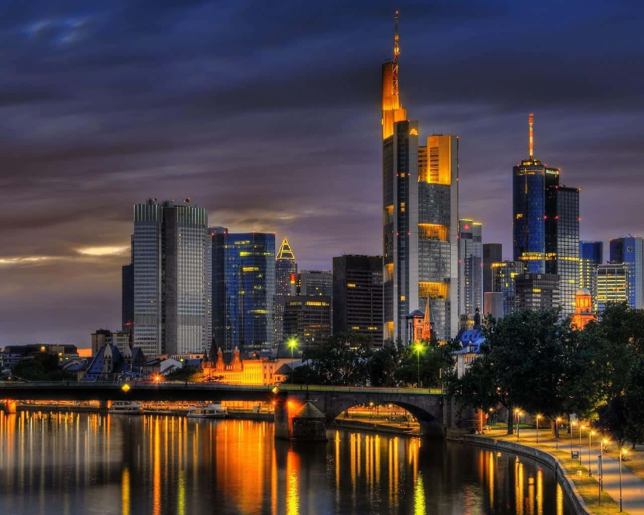 Germany 桌布 壁紙 — 黃昏時分充滿活力的城市天際線，燈火通明的摩天大樓倒映在下方平靜的河流中。