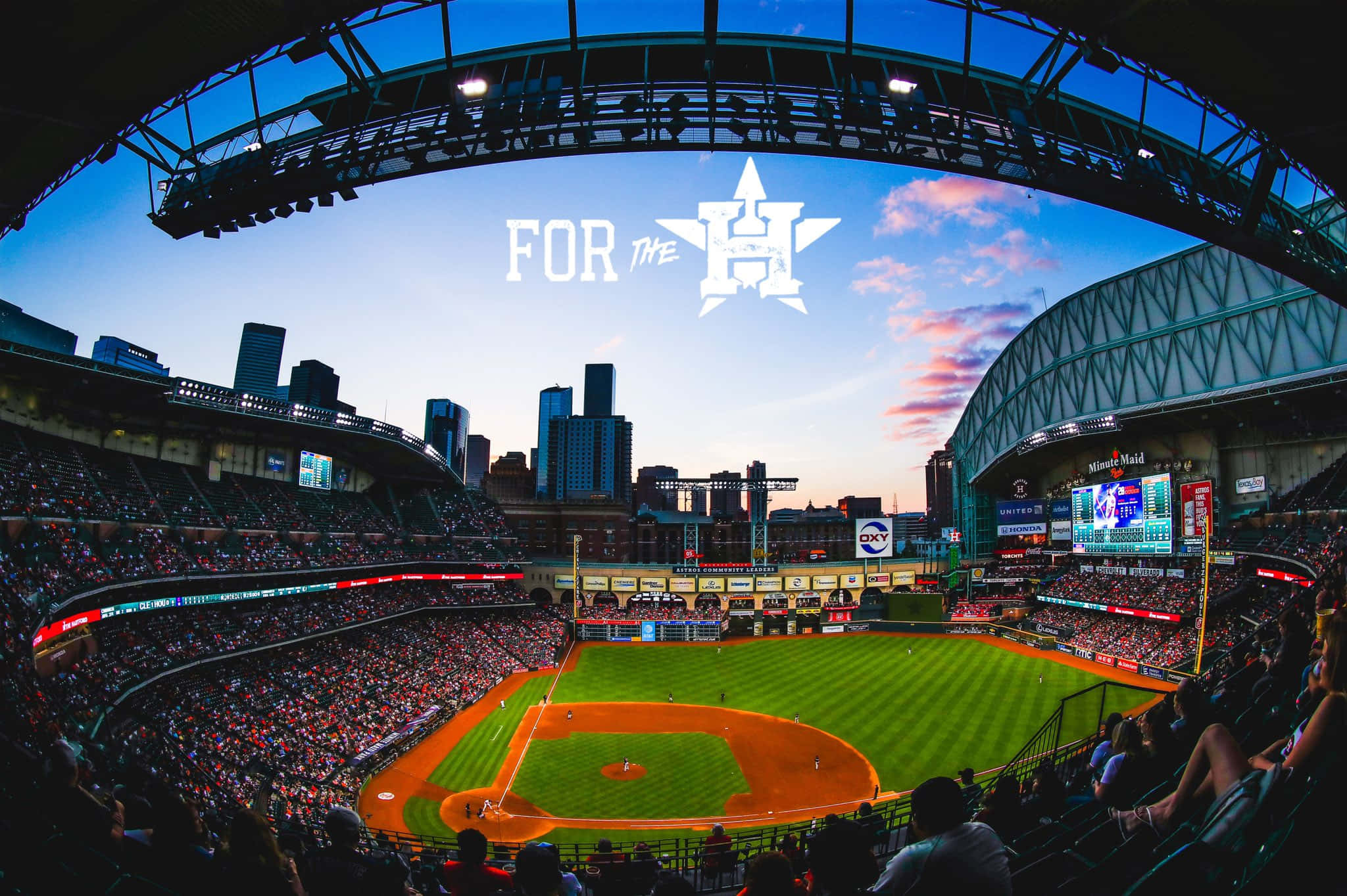 Astros 桌布 壁紙 — 黃昏時分充滿活力的棒球場，球迷在暮色天空下歡呼，背景是城市天際線。