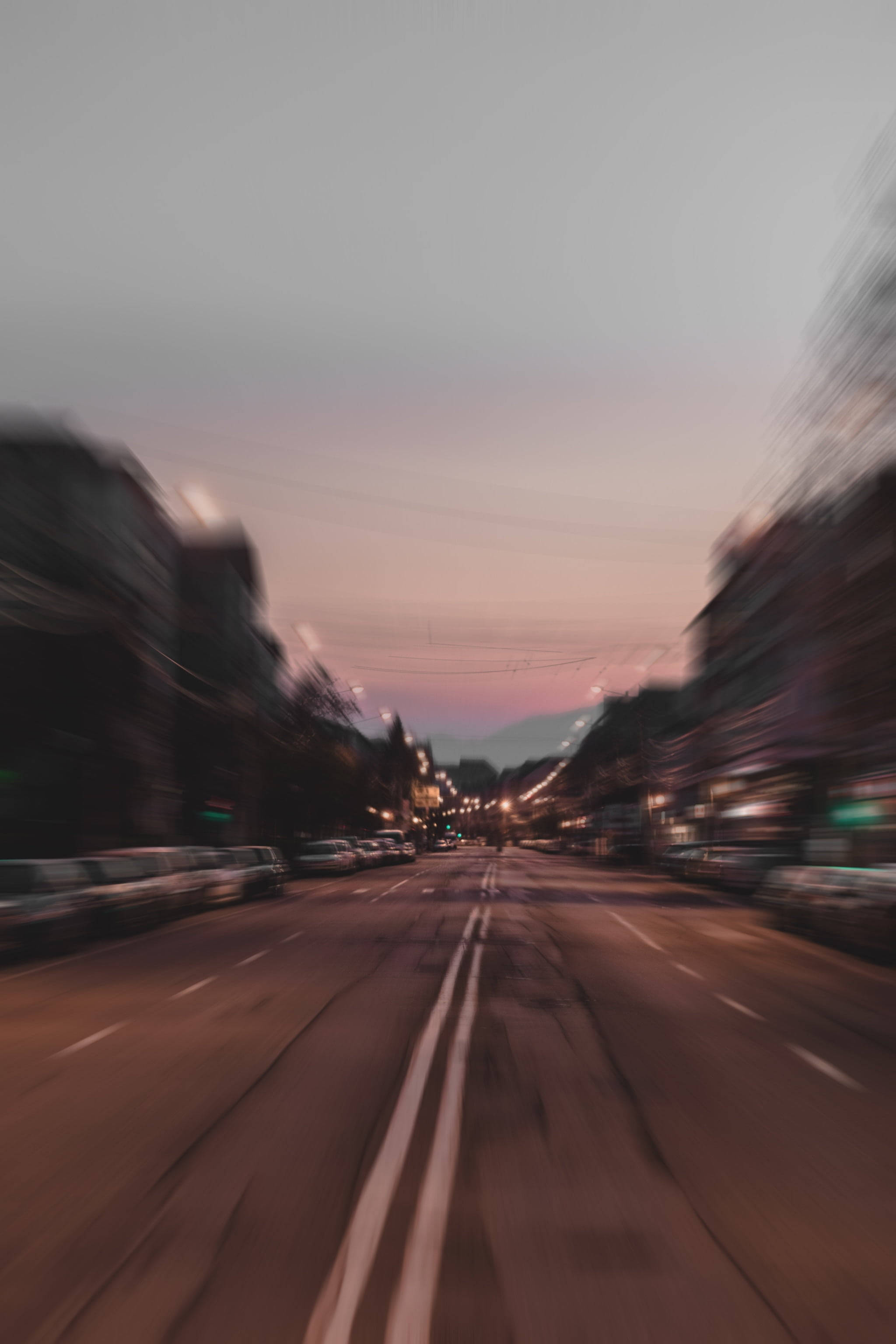 speeding car 桌布 壁紙 — 黃昏時分動態模糊的城市街道，帶有流動燈光和柔和粉紅色的天空。