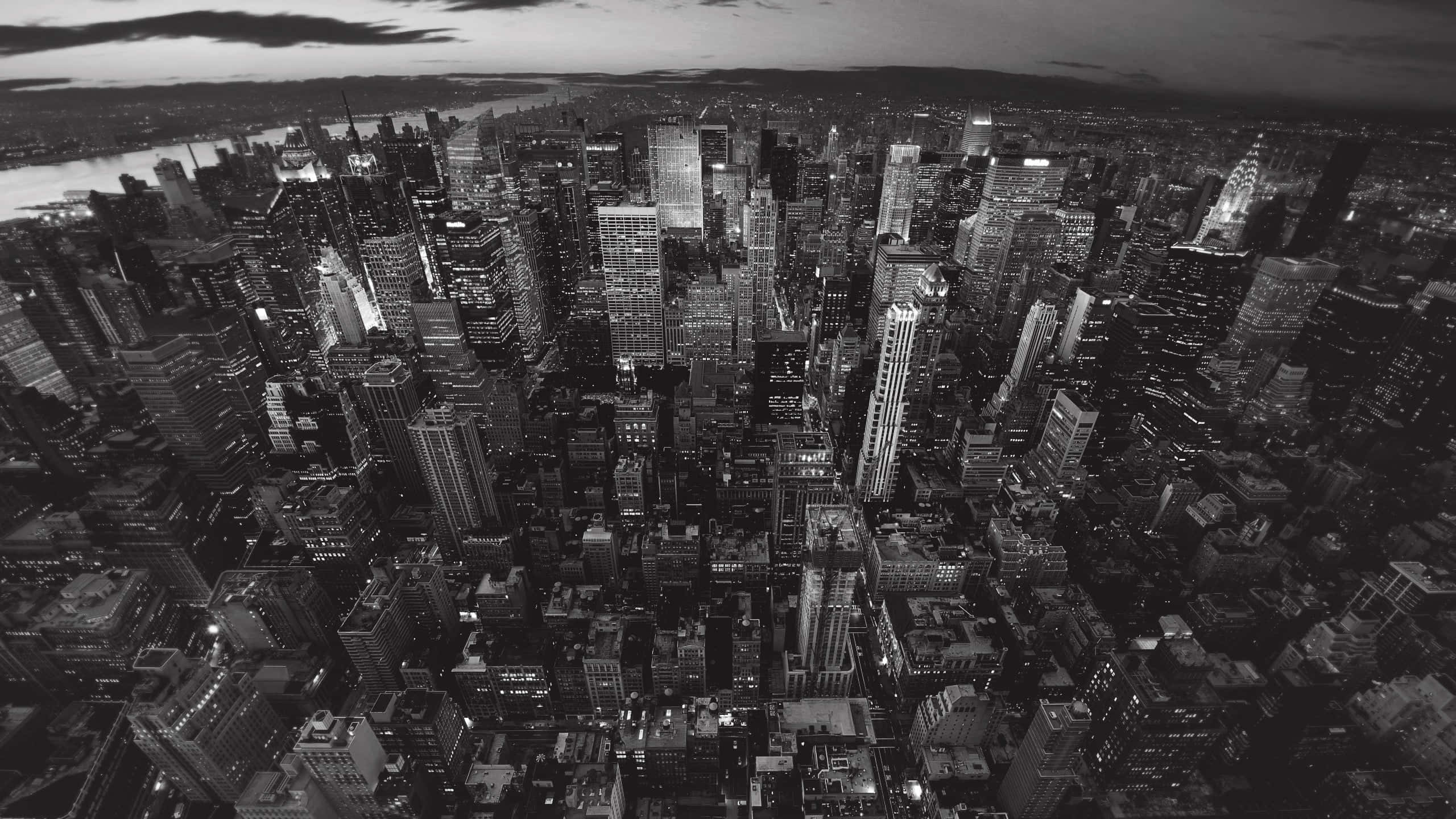 Black And White Cityscape 桌布 壁紙 — 黃昏時分密集城市景觀的黑白航拍圖，顯示了燈火通明的摩天大樓和蜿蜒穿過城市範圍的河流。