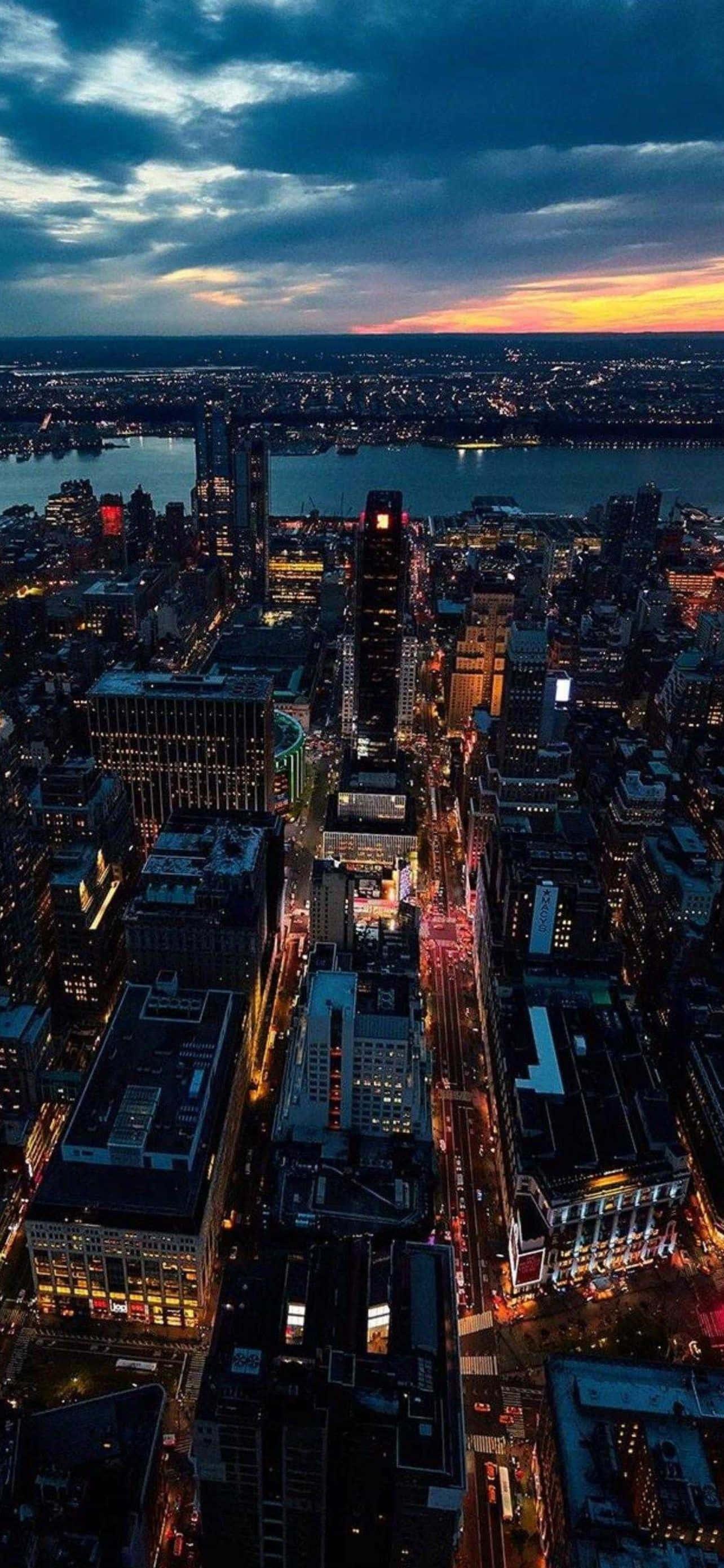 型格 iPhone 壁紙 桌布 壁紙 — 黃昏時分廣闊城市景觀的鳥瞰圖，閃爍的摩天大樓和河流映照著逐漸褪色的橙色日落。