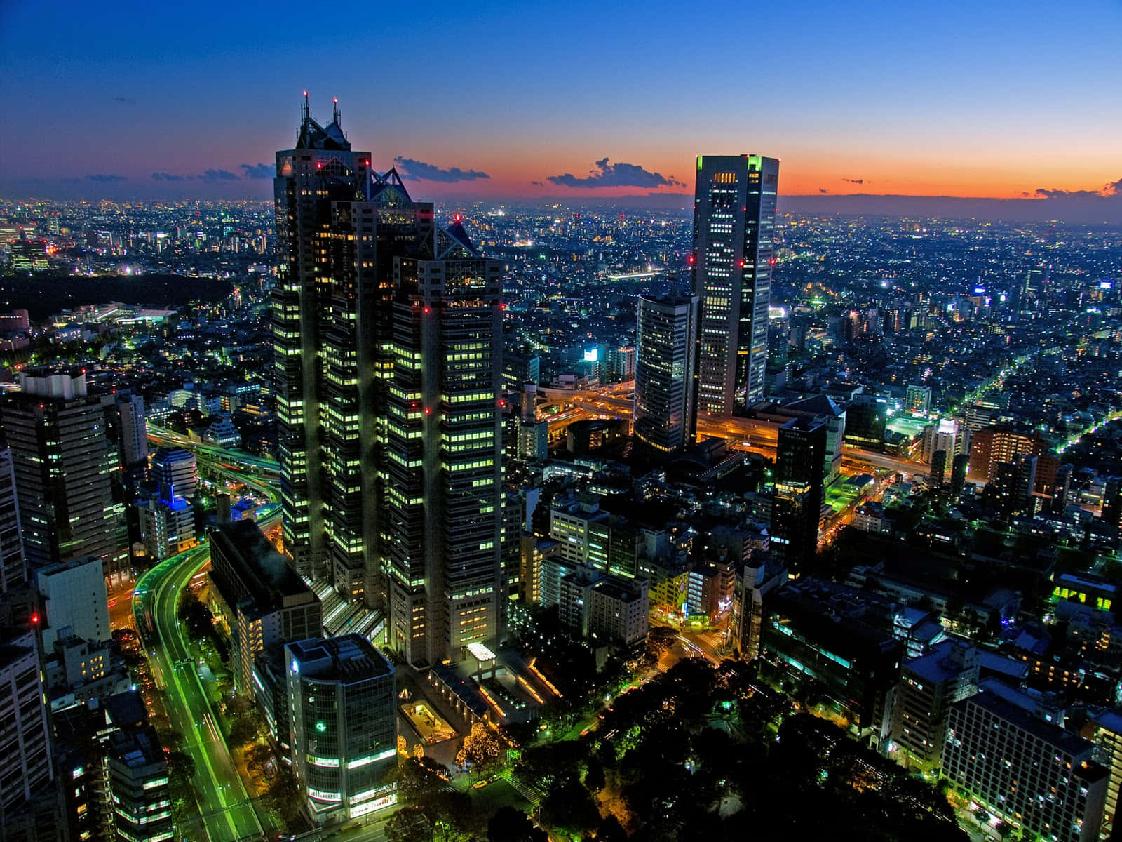 東京 桌布 壁紙 — 黃昏時分廣闊城市景觀的鳥瞰圖，高聳的摩天大樓在漸變的天空下閃耀。