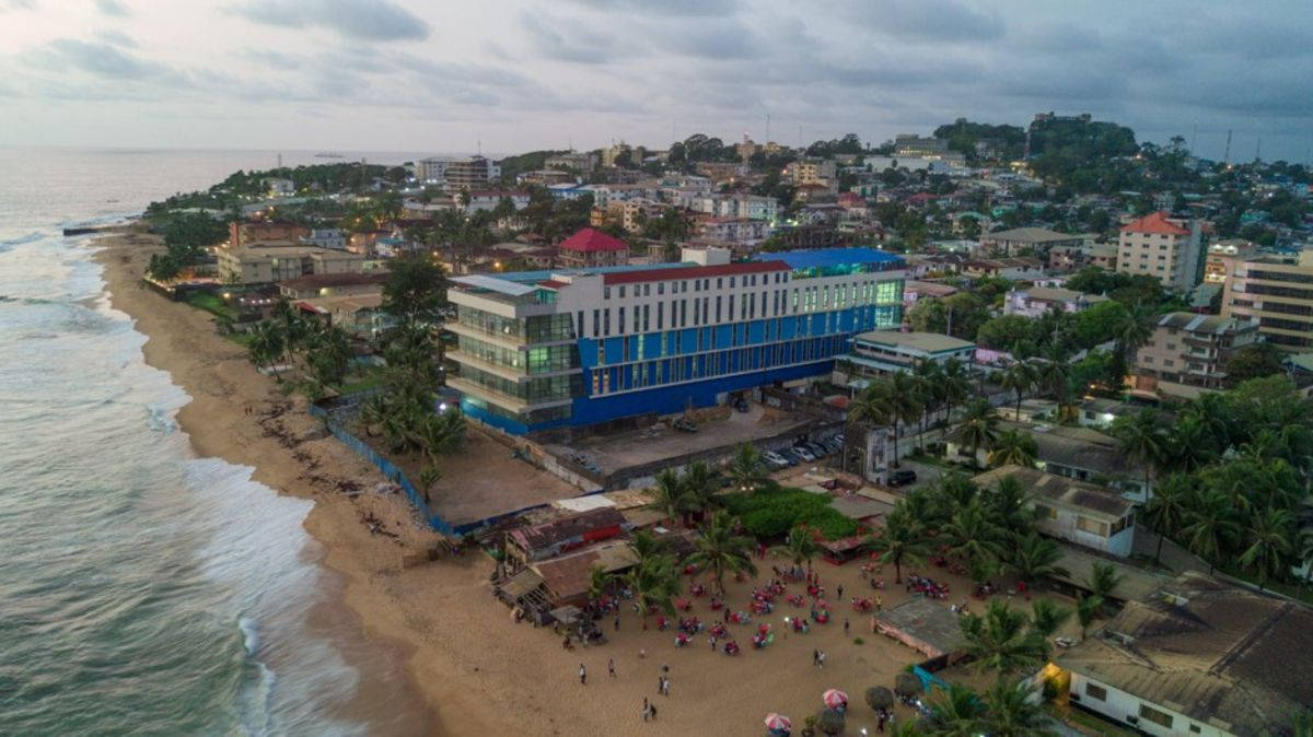 Liberia 桌布 壁紙 — 黃昏時分沿海小鎮的鳥瞰圖，沙灘和棕櫚樹旁有一座大型藍色酒店。