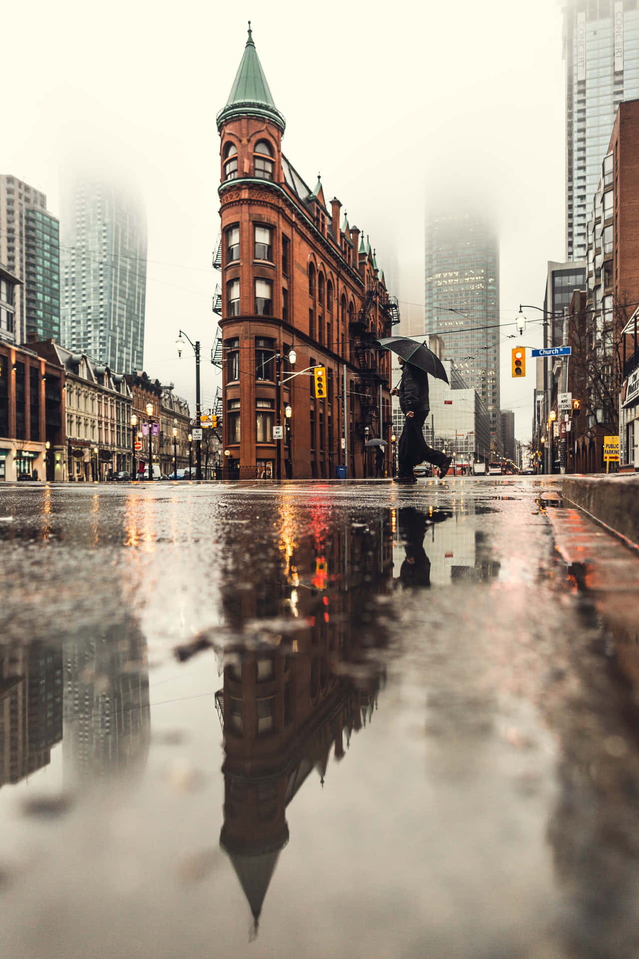撐傘的人走在雨中的城市街道上，水坑中有建築物倒影。