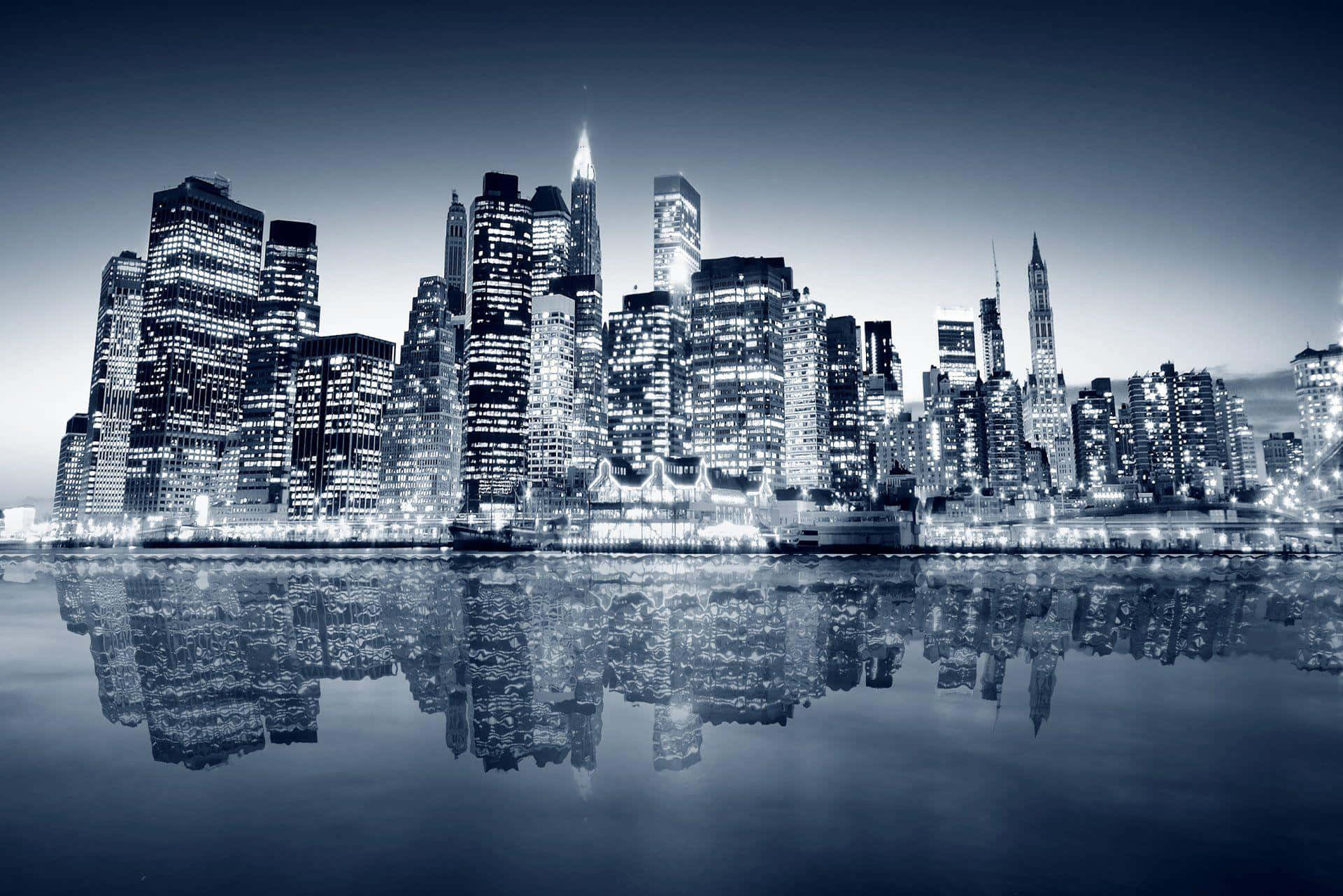 Buildings 桌布 壁紙 — 黃昏時分的單色城市天際線，摩天大樓完美倒映在平靜的水面上。