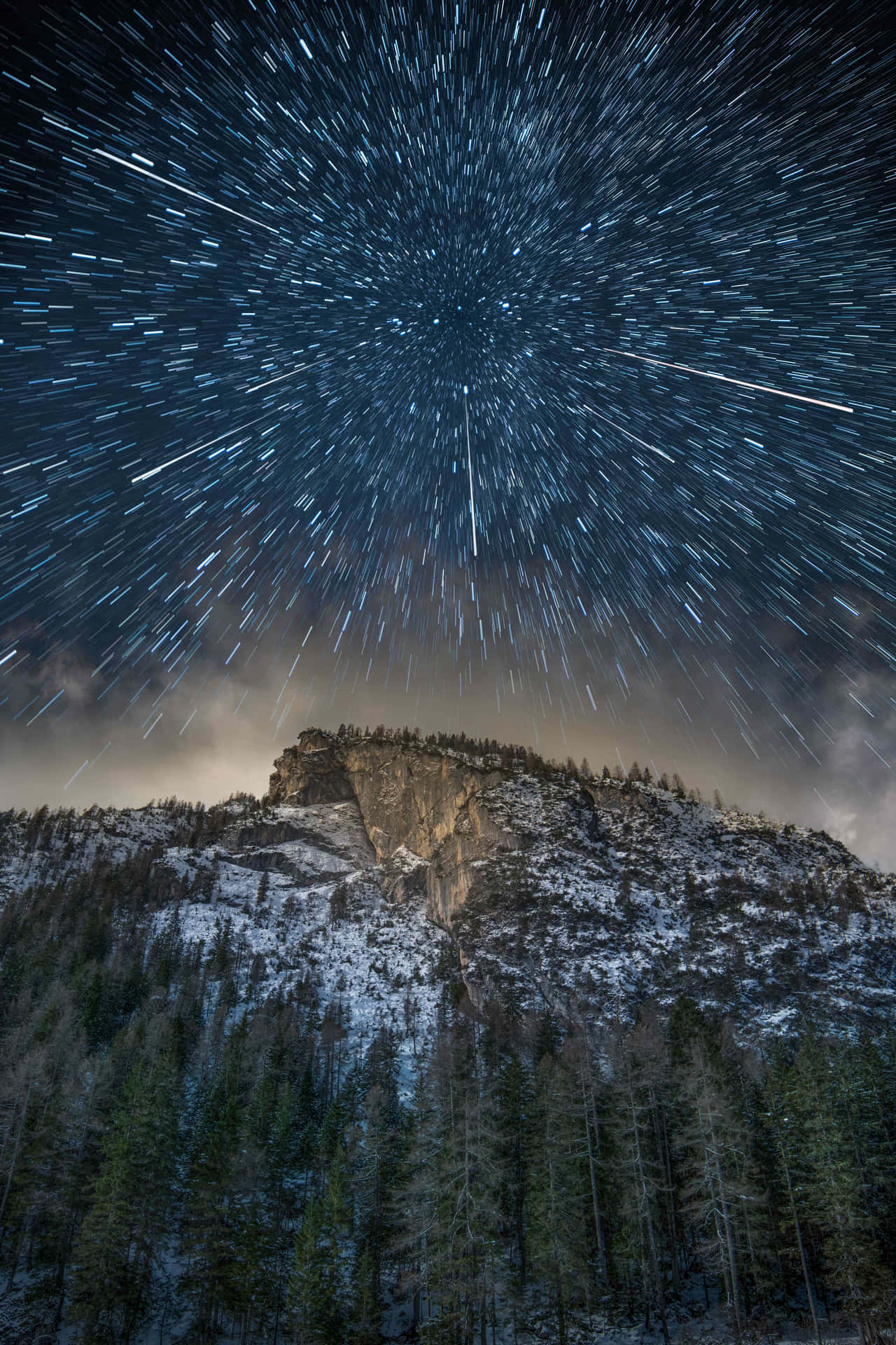 夜間積雪的山峰和森林上空的星軌
