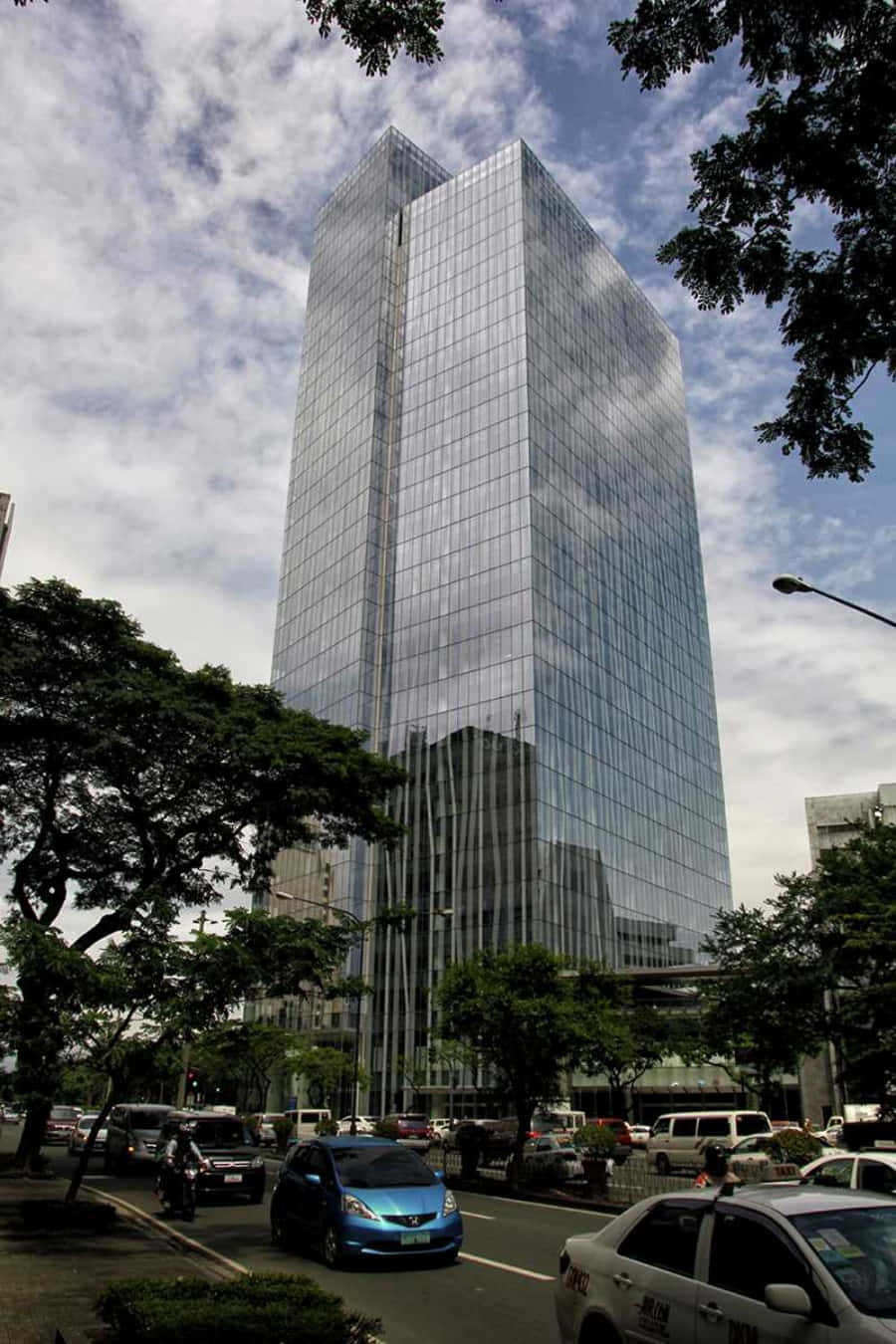 繁忙城市街道上高聳的玻璃摩天大樓，有樹木和汽車。