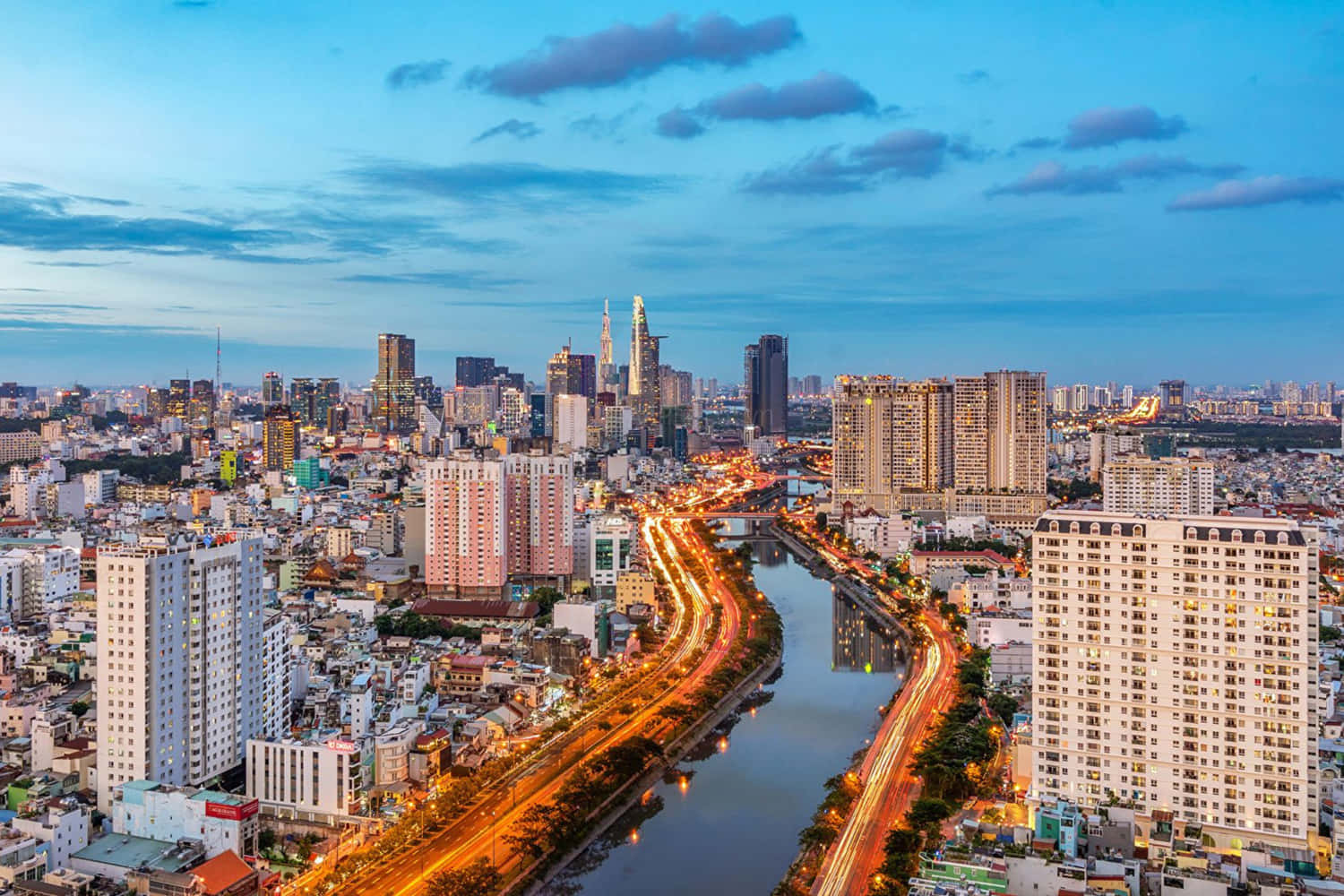 Vietnam 桌布 壁紙 — 黃昏時分繁忙城市的鳥瞰圖，沿著蜿蜒穿過高樓大廈和密集城市街區的河流，有發光的交通痕跡。