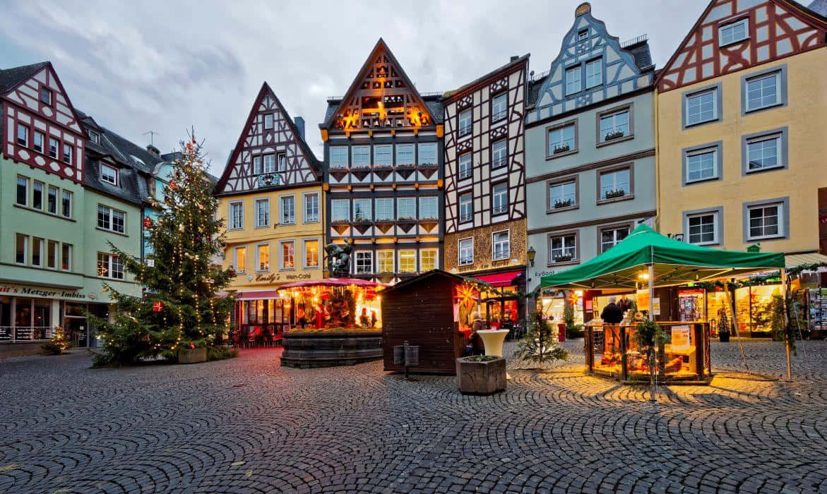 Germany 桌布 壁紙 — 黃昏時分迷人的歐洲小鎮廣場，半木結構建築在裝飾聖誕樹和節日市場攤位旁溫暖地閃耀。