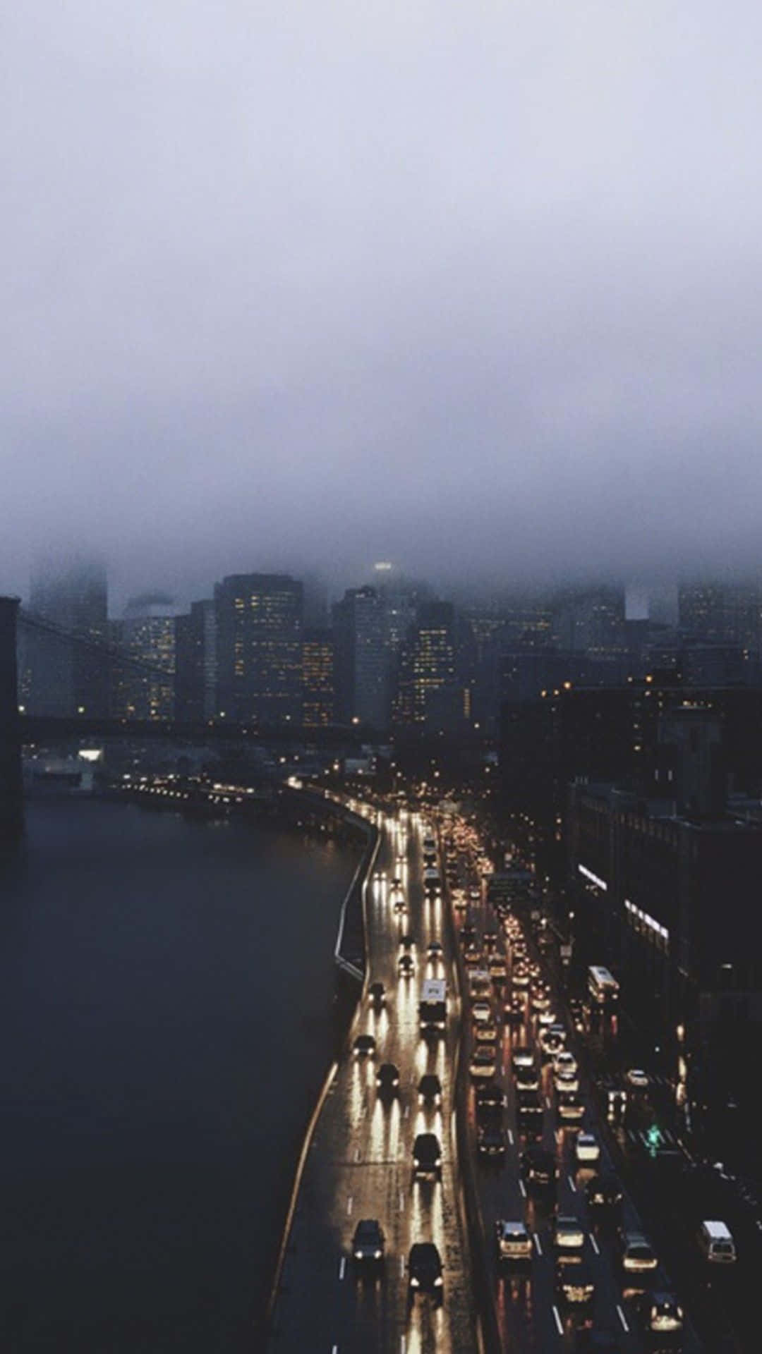 Aesthetic Grunge Phone 桌布 壁紙 — 黃昏時分雨濕的城市高速公路，發光的車頭燈穿過霧氣瀰漫的城市天際線。