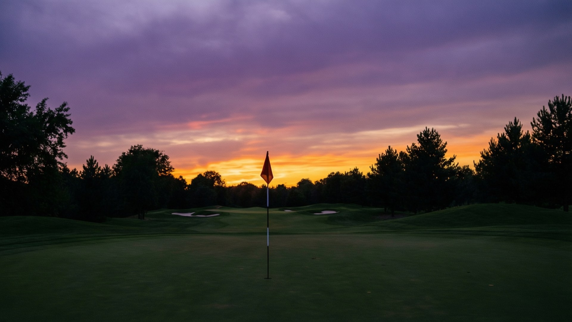 夕陽下果嶺上的高爾夫球旗，紫色和橙色天空與樹木剪影