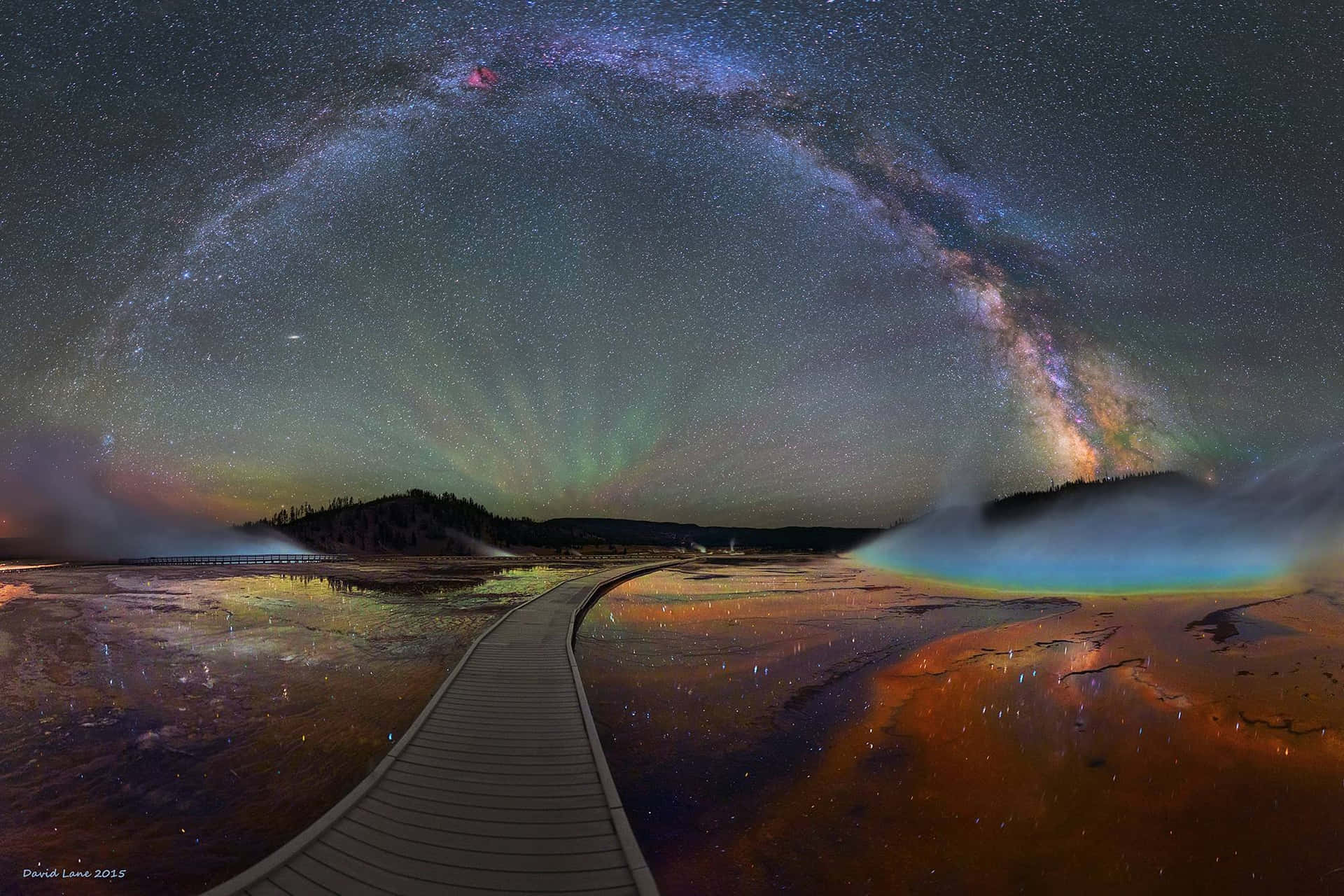 步道蜿蜒穿過發光的地熱池，在星空下，銀河和極光閃耀。