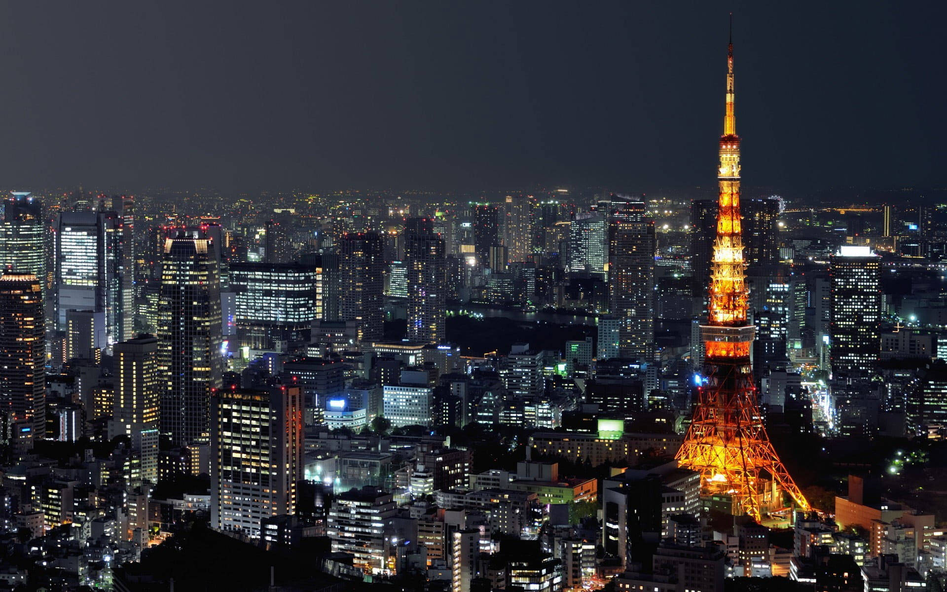 黃紅橙色東京塔 壁紙 — 東京鐵塔在漆黑的天空中溫暖地發光，城市燈光照亮了下方廣闊的城市景觀。