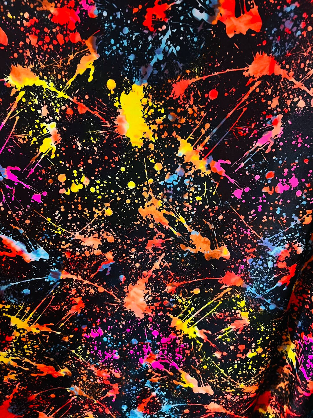 黑色布料上的螢光顏料飛濺形成大膽的抽象圖案。