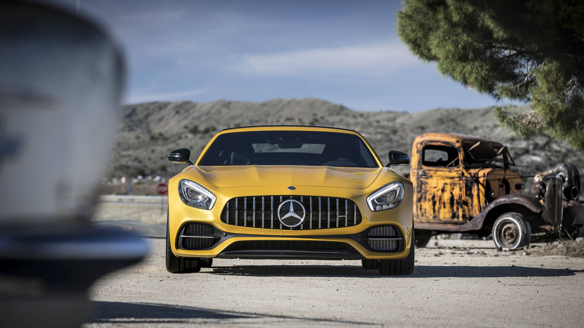 黃色 Mercedes 跑車停在一輛生鏽的卡車旁，位於沙漠景觀中。