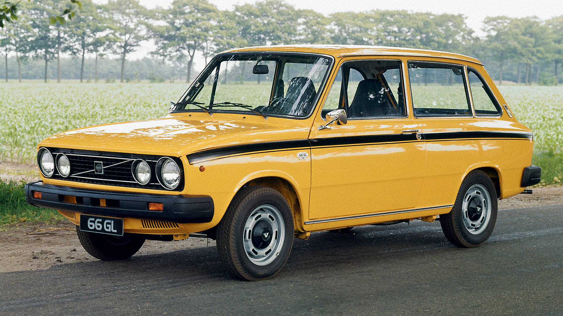黃色66款沃爾沃iPhone照片 壁紙 — 一架鮮黃色復古Fiat 126p旅行車停泊在鄉村道路上，旁邊是長滿高大綠色植物的田野。