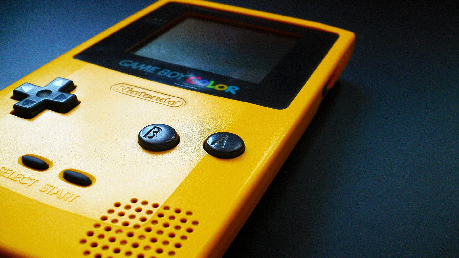 黃色Game Boy Color特寫 壁紙 — 一個黃色Game Boy Color的特寫，帶有黑色按鈕和屏幕，放置在深色表面上。