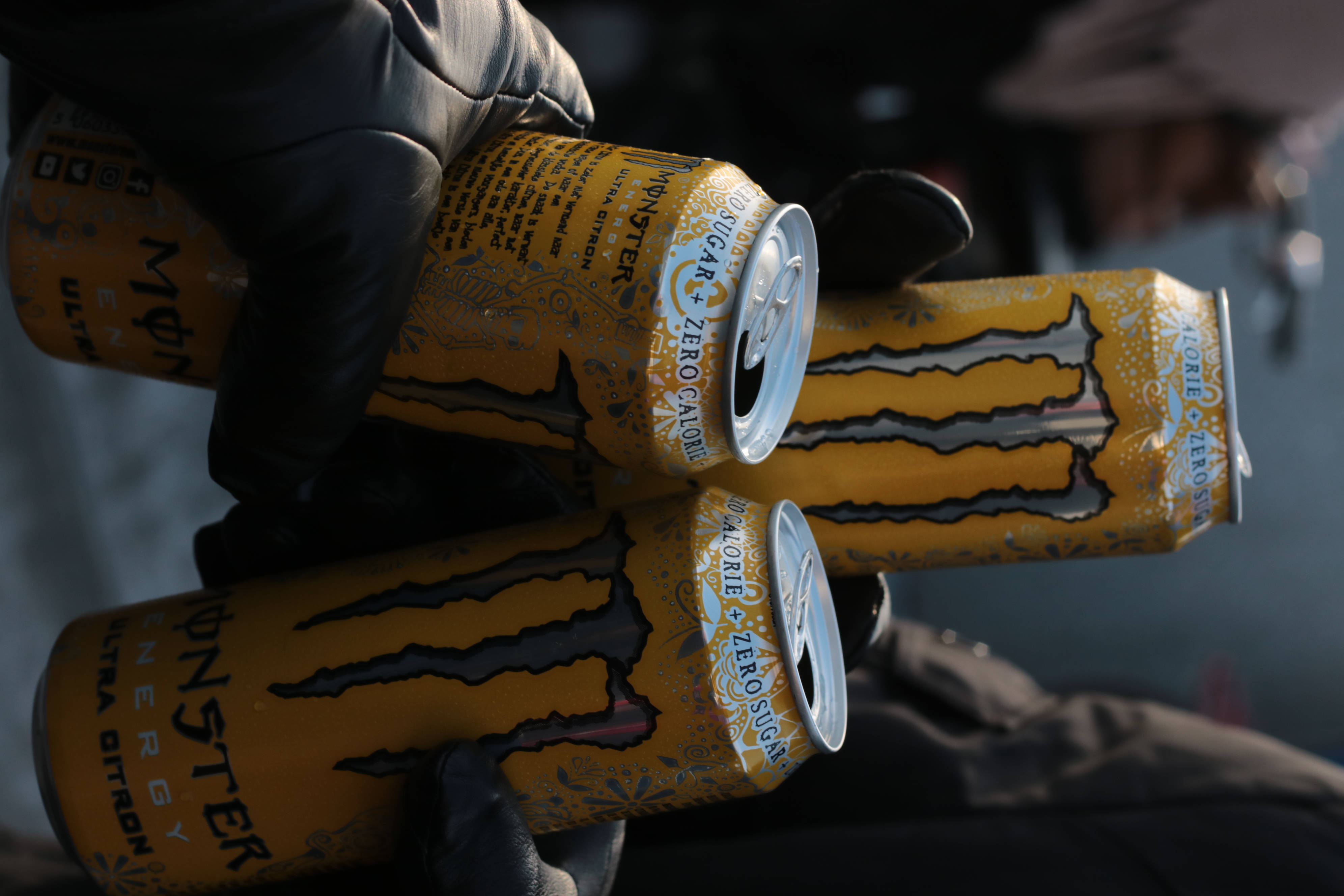 黃色Monster Energy能量飲料罐 壁紙 — 戴手套的手抓住三個黃色Monster Ultra零卡路里能量飲料罐，帶有銀色拉環和黑色爪痕。