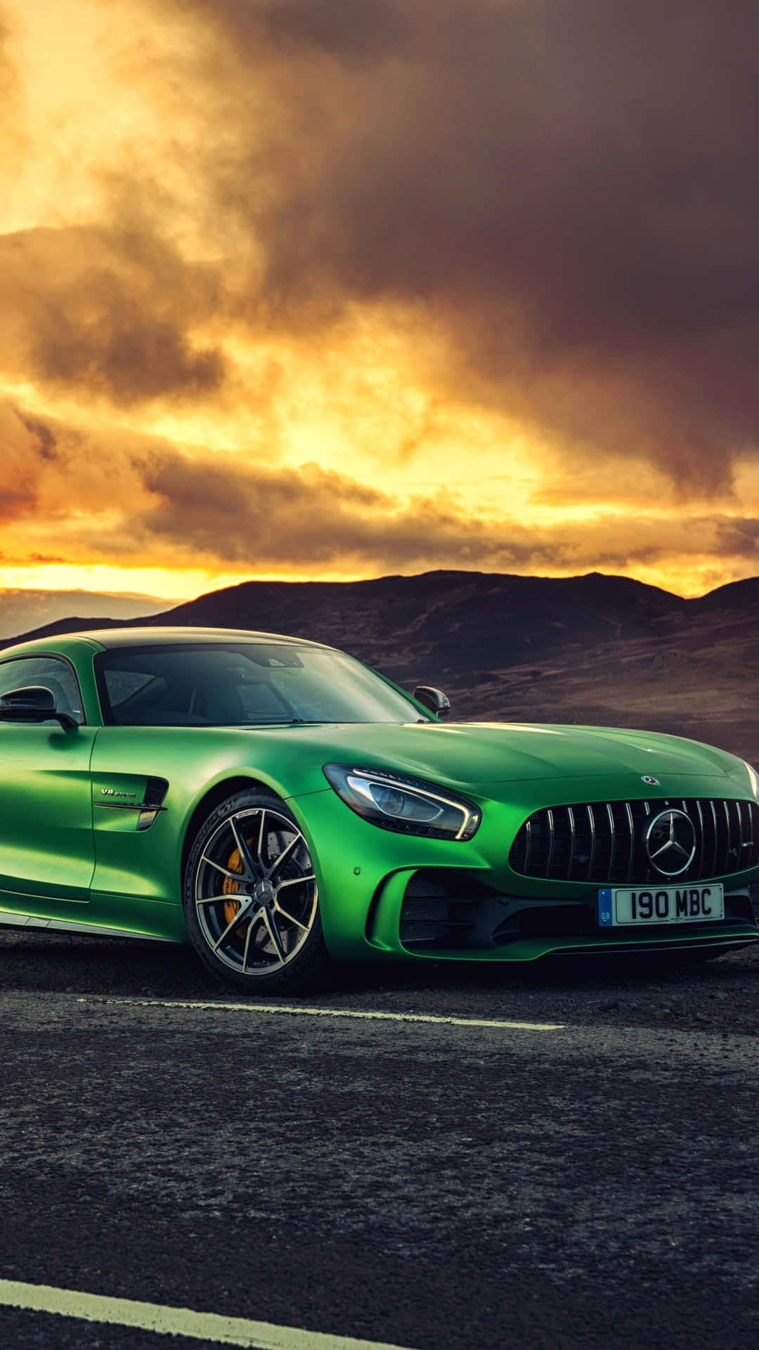 黃色天空安卓翡翠綠AMG GT-R背景 壁紙 — 一輛充滿活力的綠色 Mercedes-AMG GT 跑車停泊在道路上，背景是戲劇性的金色日落天空和起伏的山丘。