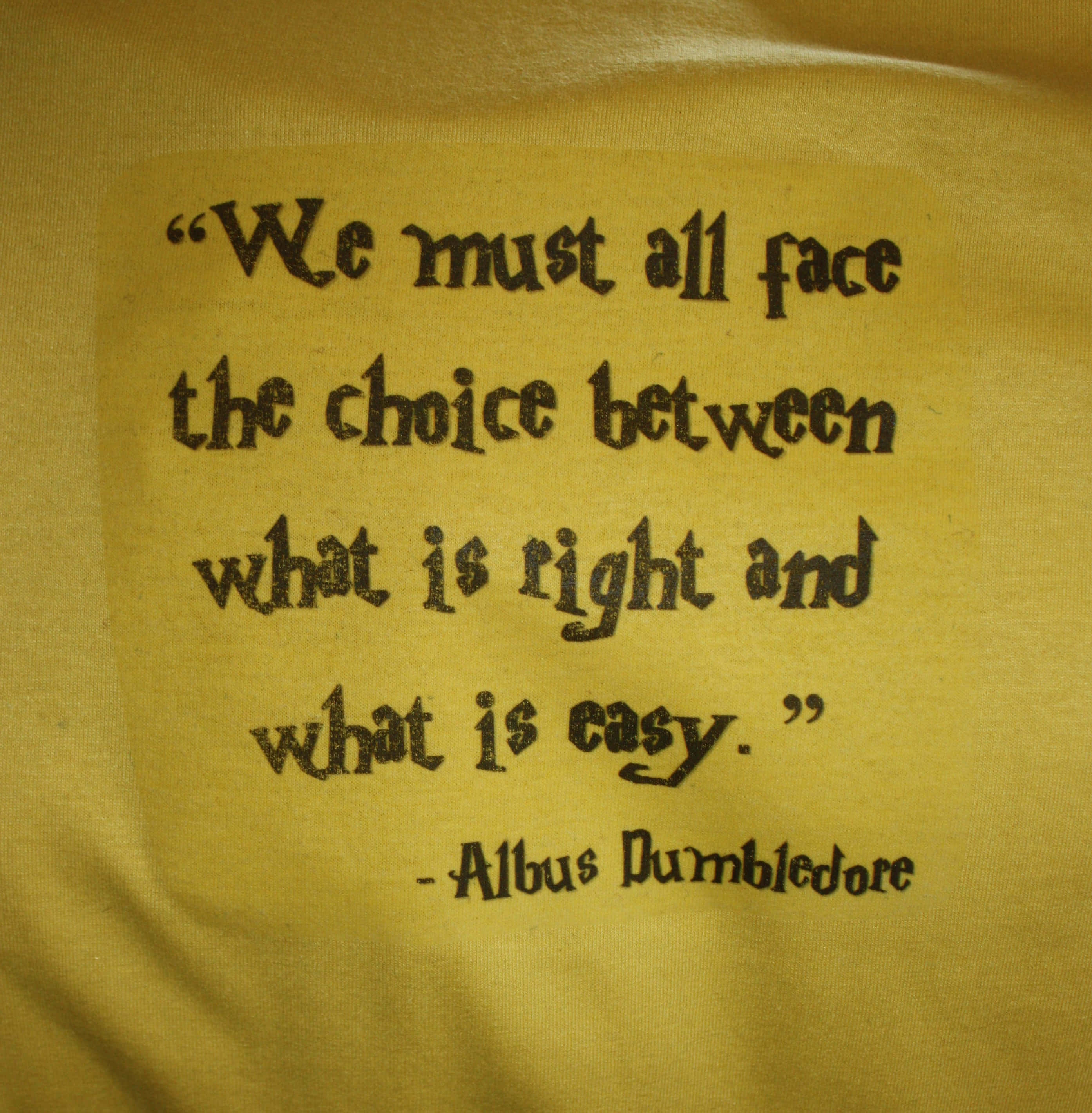 Harry Potter Quotes 桌布 壁紙 — 黃色布料特寫，上面有阿不思·鄧不利多關於選擇正確而非容易的黑色刺繡名言。