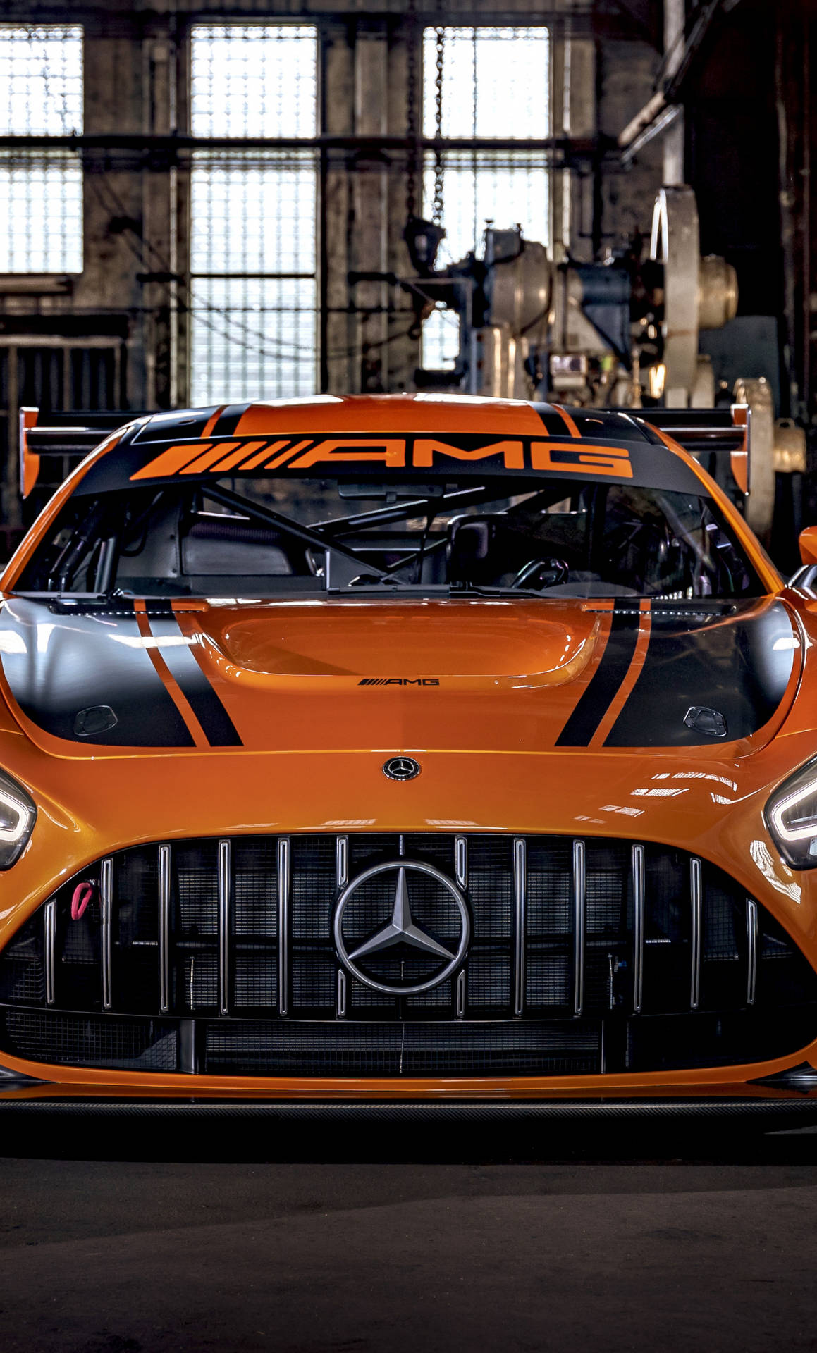 工業車庫中的橙色 Mercedes-AMG 賽車，帶有金屬格柵和賽車條紋。
