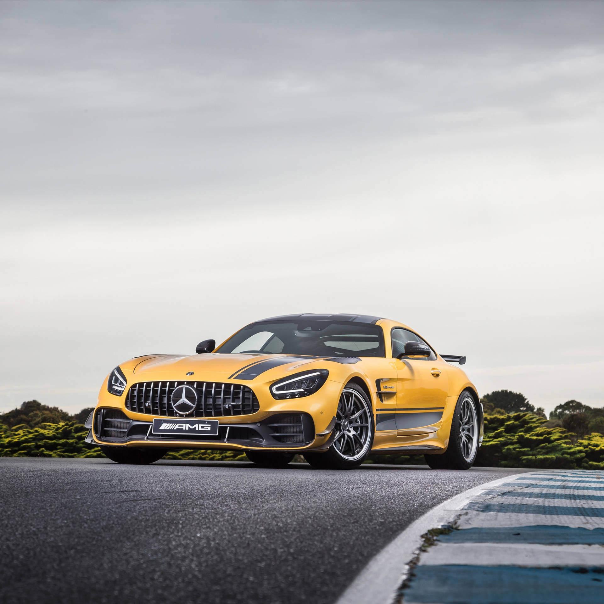 黃色 Mercedes-AMG GT R 在賽道上，配有藍色路緣石和綠色灌木叢。