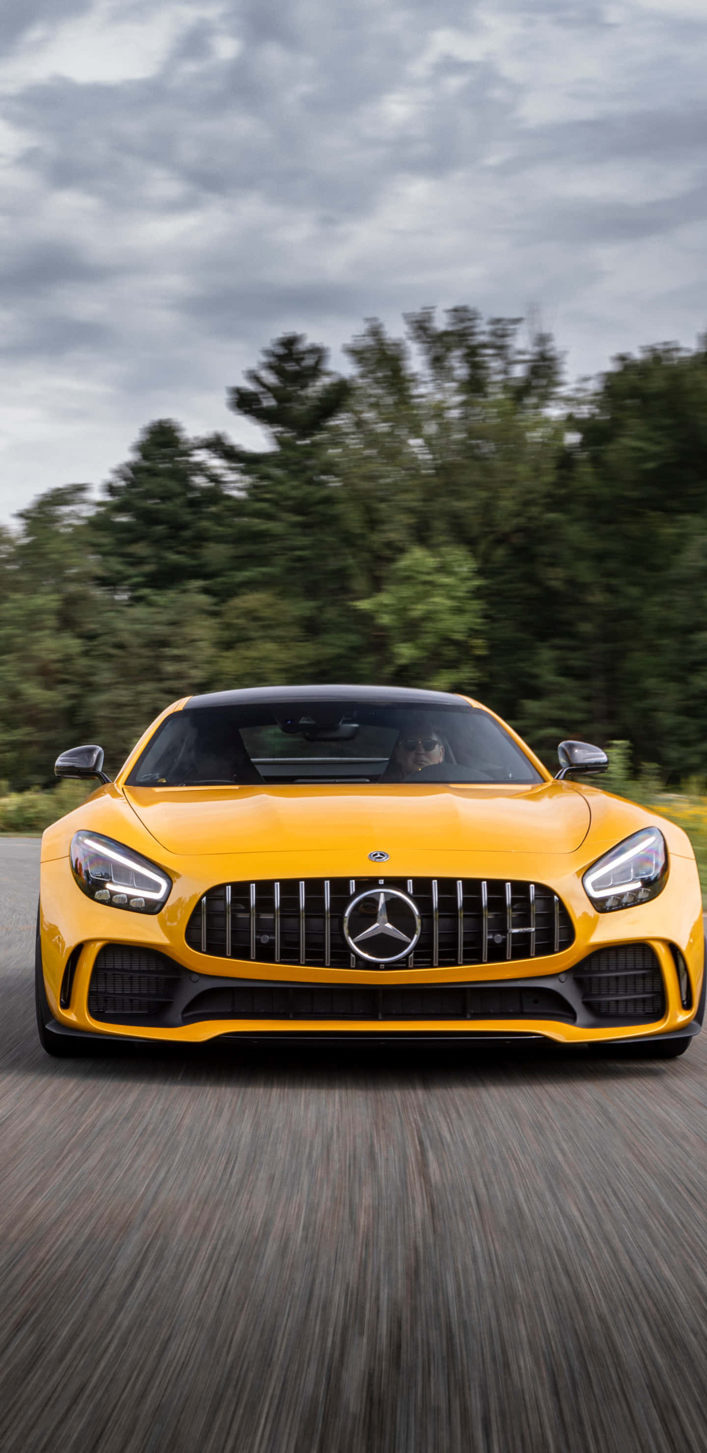 黃色梅賽德斯正面視圖 Pixel 3XL AMG GT-R 背景 壁紙 — 一輛鮮黃色的 Mercedes-AMG GT 跑車在陰天下行駛在森林環繞的道路上。