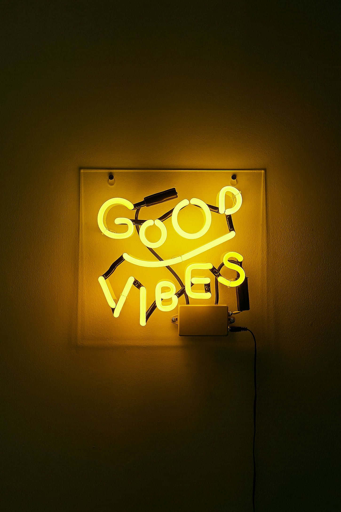 黃色美學LED標誌圖 壁紙 — 一個發光的黃色霓虹燈牌，上面寫著「GOOD VIBES」和一個笑臉，在黑暗的牆壁上投射出溫暖的光芒。
