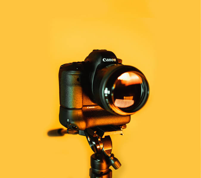 黑色Canon DSLR相機在三腳架上，黃色背景