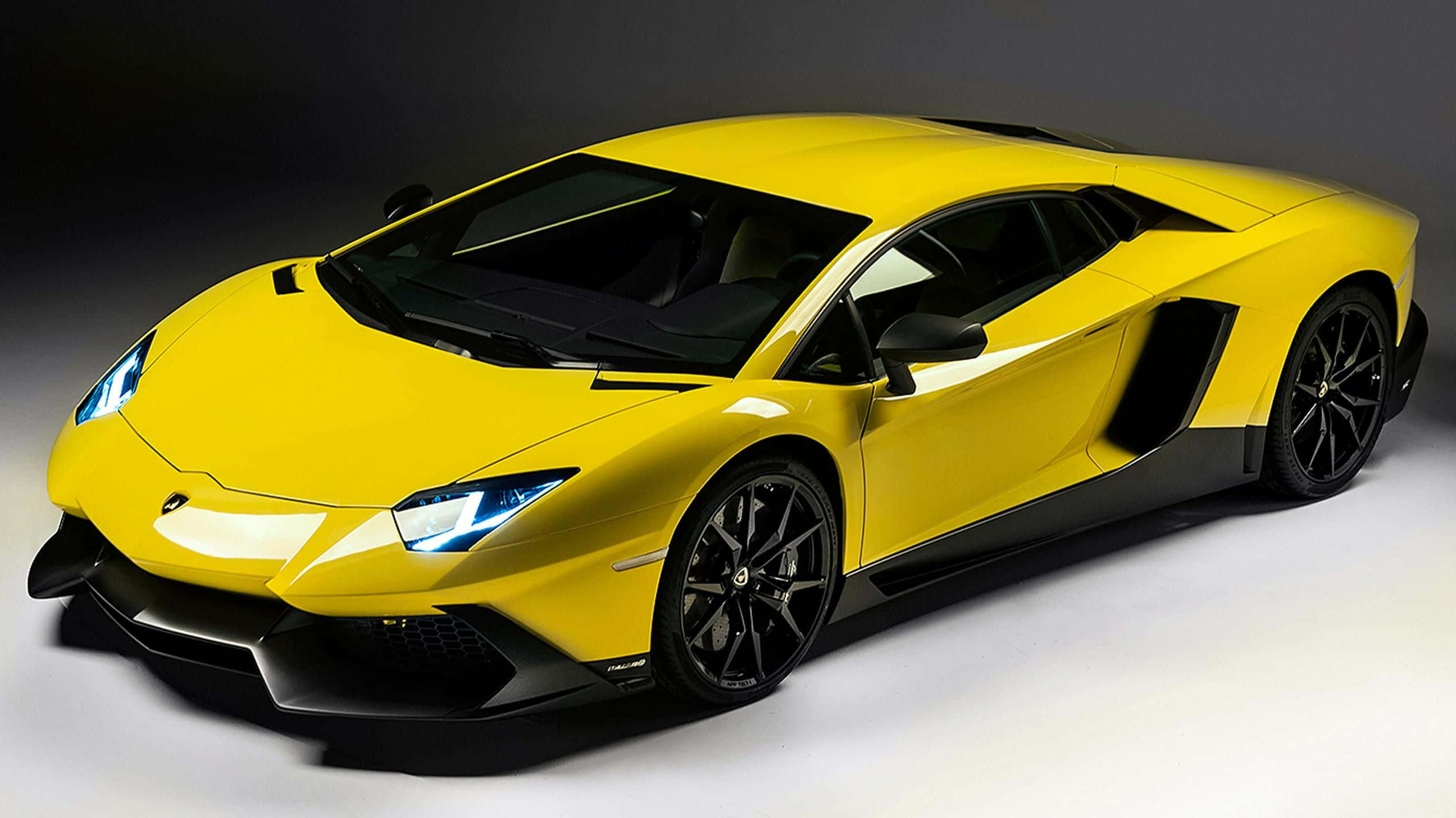 黃色蘭博基尼高速跑車 壁紙 — 一輛充滿活力的黃色林寶堅尼Aventador跑車，帶有黑色飾邊和發光車頭燈，在深色工作室背景前擺拍。