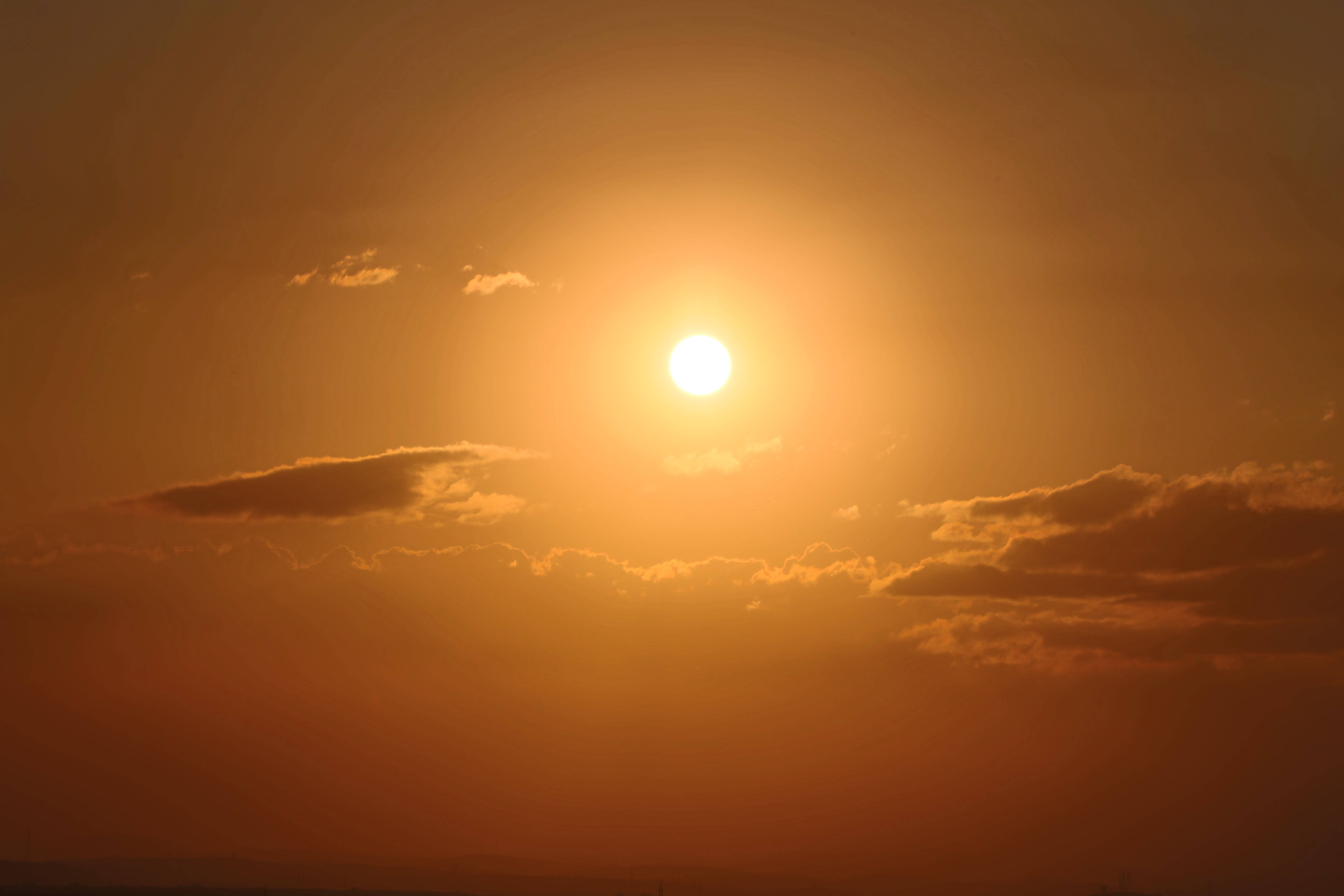 黃金時刻最佳桌面 壁紙 — 夕陽時分，溫暖的橙色天空中，一輪燦爛的太陽穿過散落的雲層，散發出強烈的光芒。