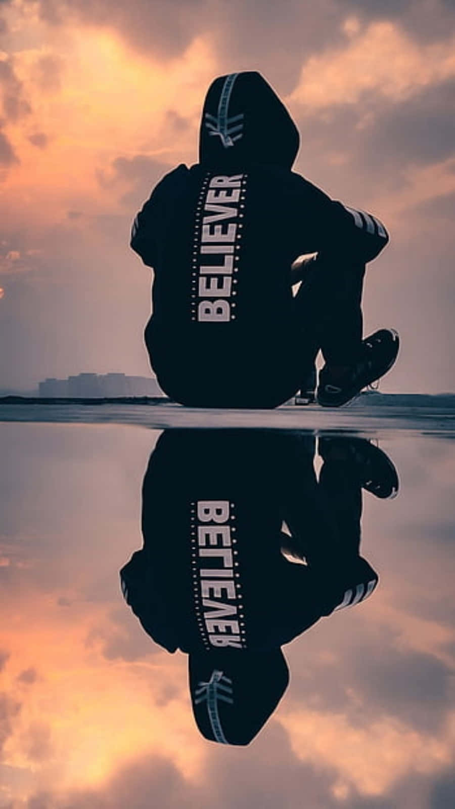 穿著印有「BELIEVER」文字的連帽衫的人的剪影，坐在水邊，帶有日落倒影。