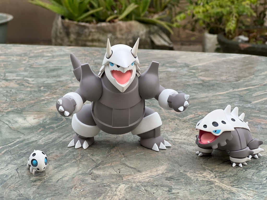 黃金時刻的阿龍壯麗風景 壁紙 — 三隻 Rhyperior 進化系列的 Pokemon 公仔擺放在大理石桌上，背景有綠色植物。
