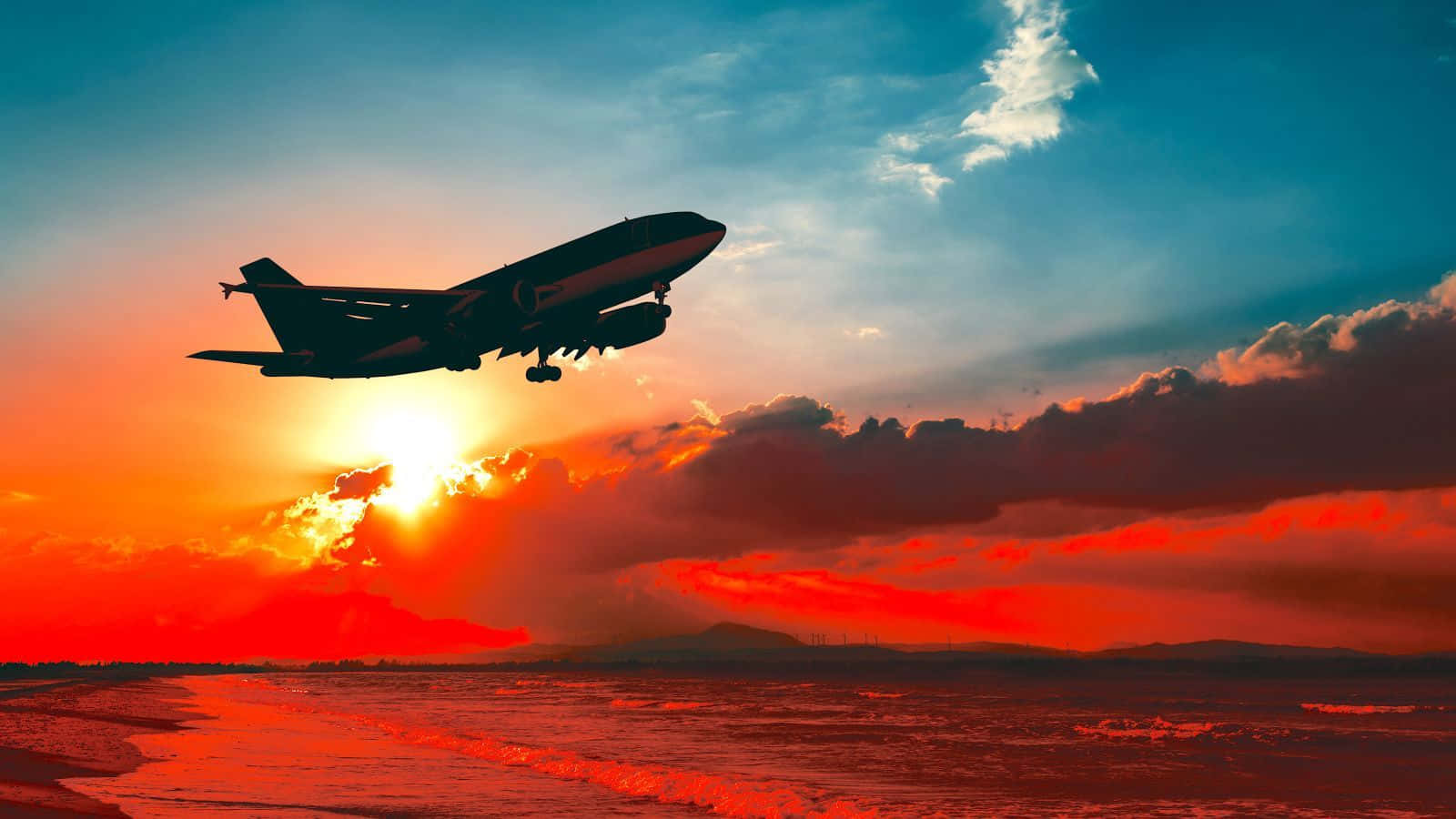 黃金時刻飛機剪影背景 壁紙 — 一架噴射飛機在沙灘上以火紅的日落為背景形成剪影，海浪拍打著海岸。
