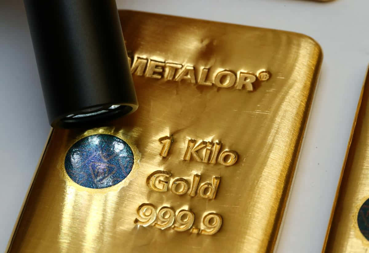 黃金條的特寫 壁紙 — 一個閃亮金條的特寫，標有「1 Kilo Gold 999.9」，帶有藍色全息封條和附近的黑色印章。