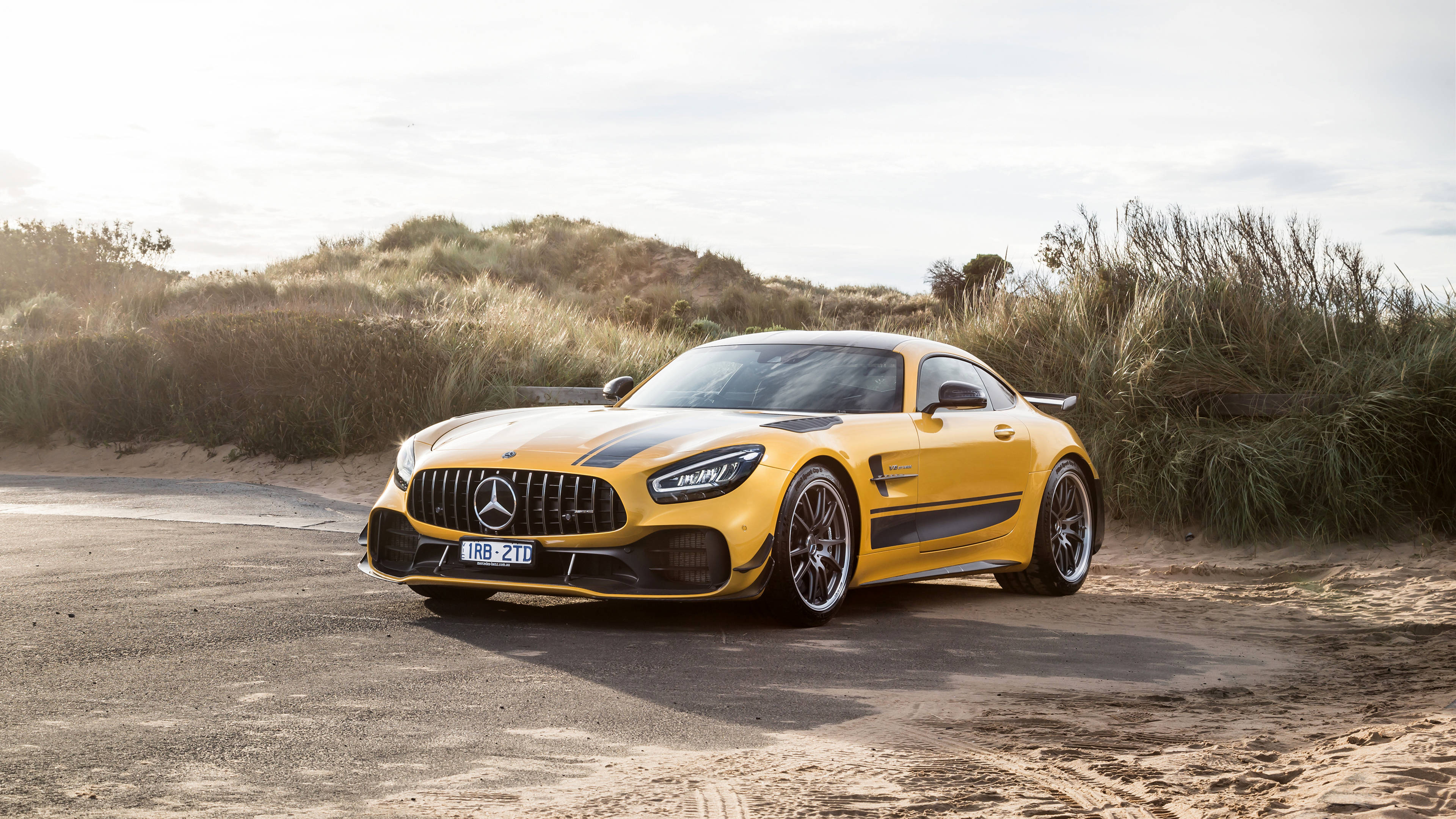 黃黑AMG停駐薩凡納草原 壁紙 — 一輛鮮黃色的 Mercedes-AMG GT Black Series 跑車停泊在沙路旁，旁邊是長滿草的沙丘，天空晴朗。