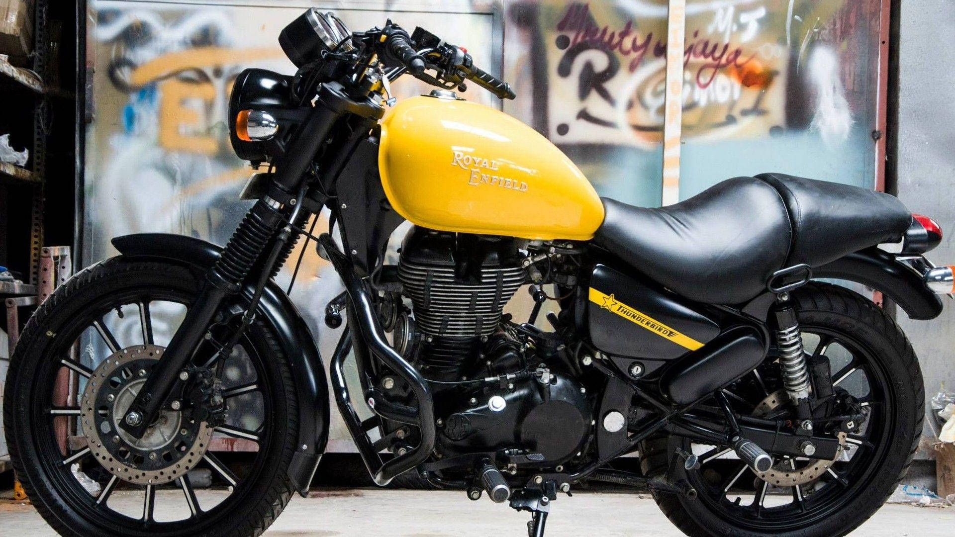 黃黑配色皇家恩菲德高畫質 壁紙 — 一輛引人注目的黃黑配色 Royal Enfield Thunderbird 電單車，停放在一個佈滿塗鴉的車庫中，配以工業照明。