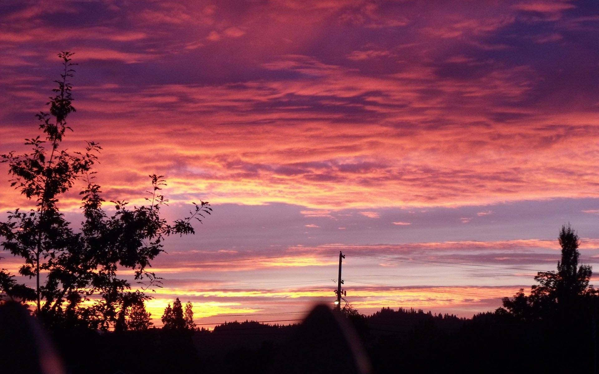 黎巴嫩紅霞雲天 壁紙 — 戲劇性的日落將天空染成火紅、紫色和橙色，映襯著剪影般的樹木和遠山。
