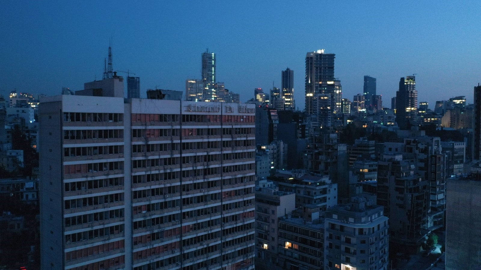 黎巴嫩高樓林立城市夜景 壁紙 — 暮色中的城市景觀，摩天大樓和住宅樓宇在深藍色天空下燈火通明。
