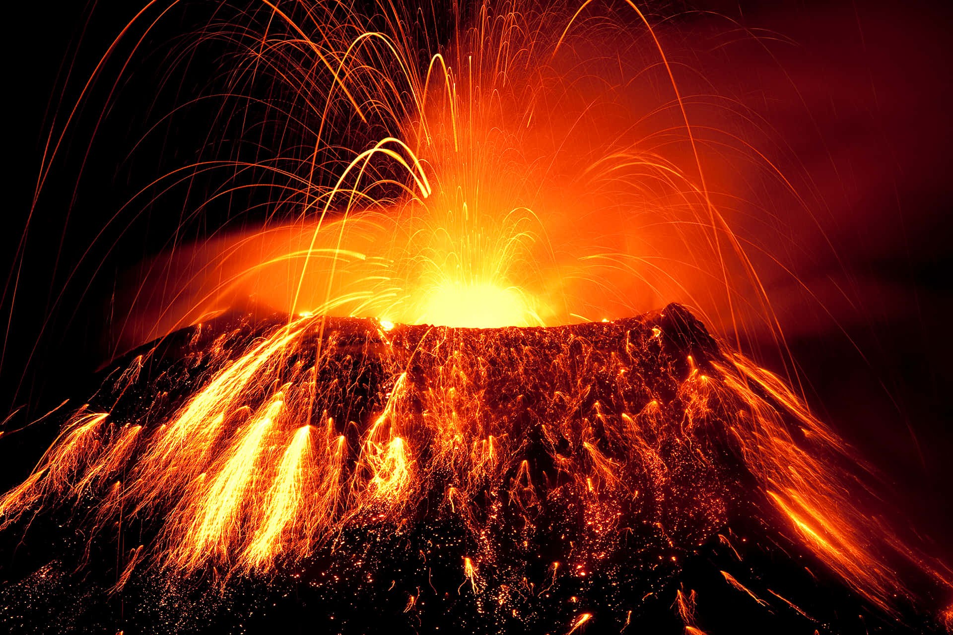 火山爆發，明亮的橙色熔岩和火花在黑暗的夜空中噴射。