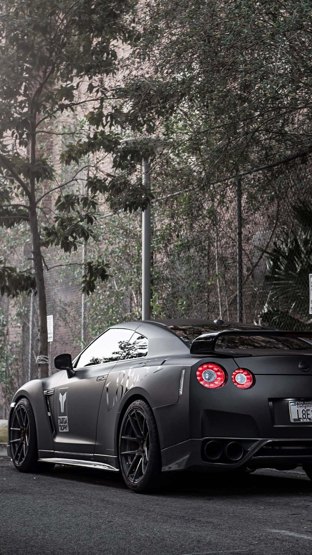 啞光黑色日產GT-R，紅色尾燈，停泊在都市環境的樹下。 — 汽車 壁紙