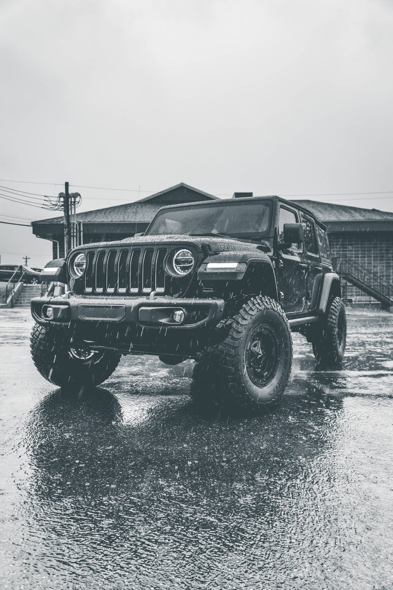 黑色Jeep Wrangler在雨中停在建築物附近的濕路面上。